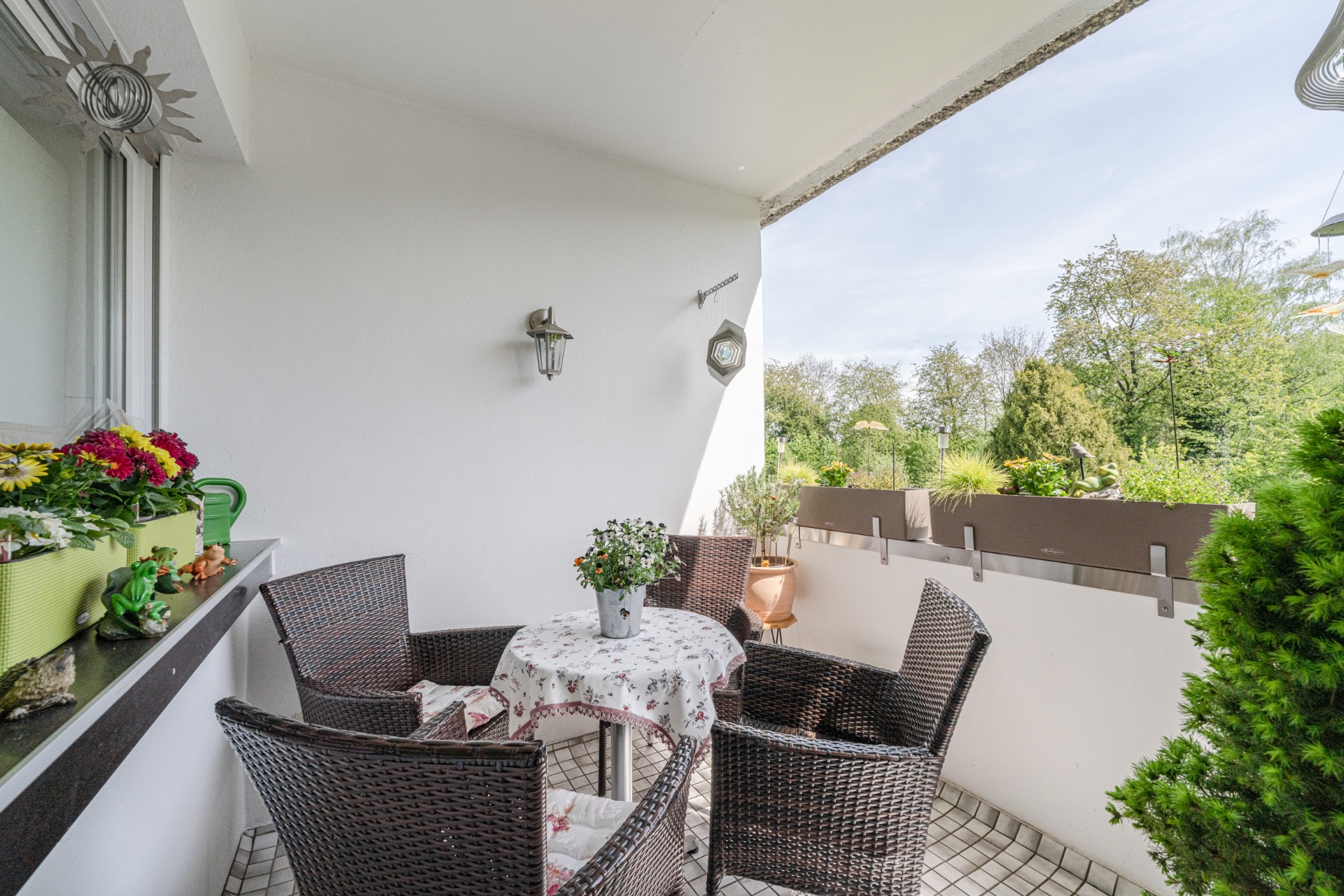 Möblierter Balkon mit vier Stühlen, rundem Tisch und Blumenpflanzen, Blick ins Grüne.