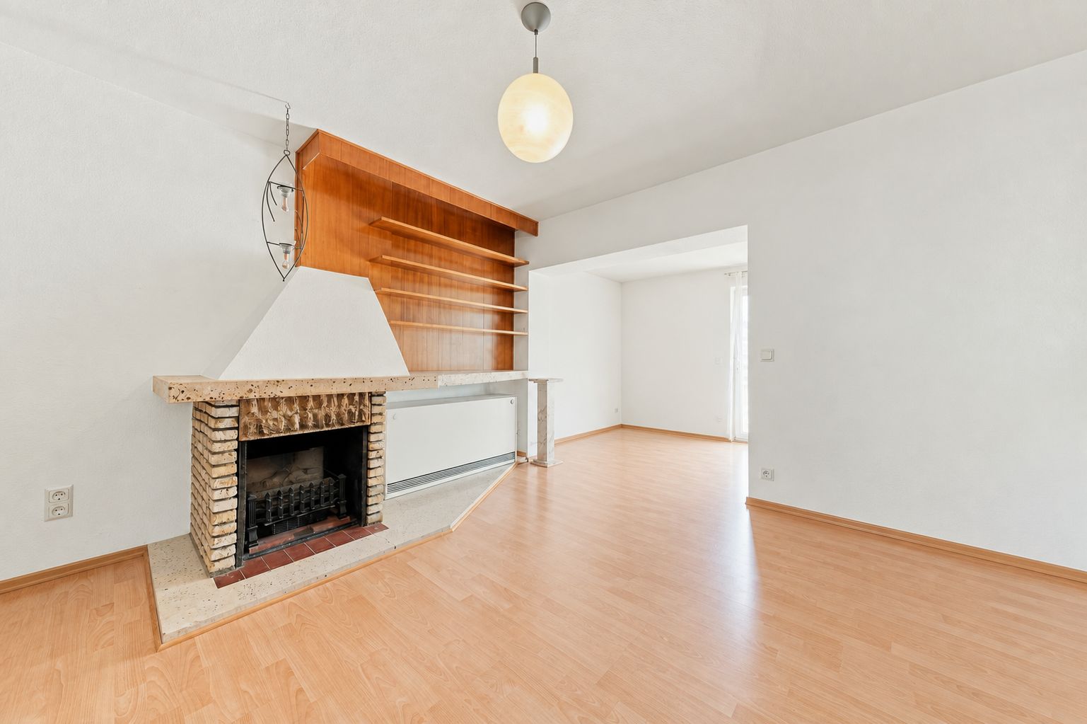 Helles Wohnzimmer mit Kamin, Holzboden und Regal an der Wand.