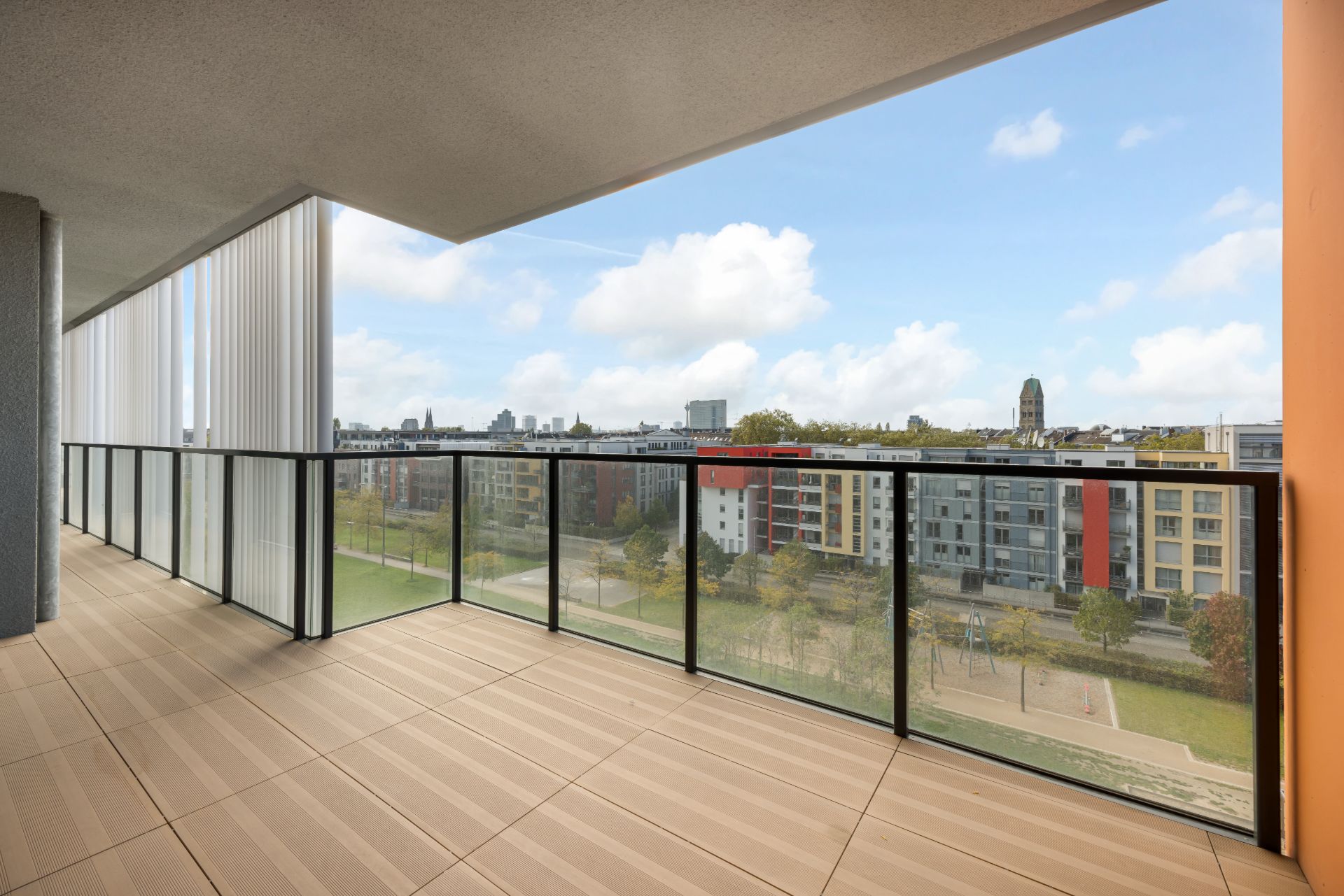 Großer Balkon mit Glasgeländer, Blick auf Wohngebäude und grüne Fläche.