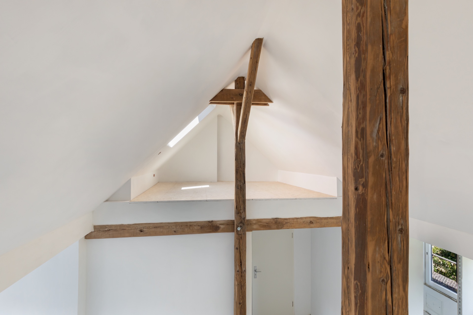 Dachgeschoss eines Hauses mit sichtbaren Holzbalken und weiß gestrichenen Wänden.