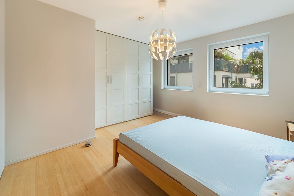 Helles Schlafzimmer mit Holzboden, Doppelbett, weißen Schränken und zwei Fenstern.
