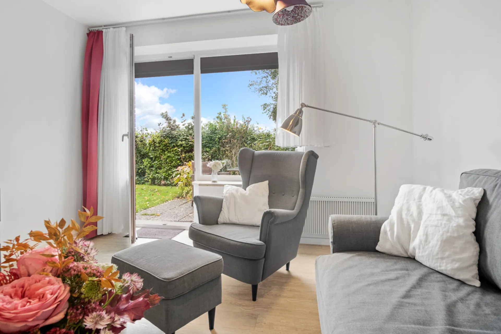 Wohnzimmer mit grauem Sessel, Sofa, Stehlampe und offenem Zugang zum Garten.