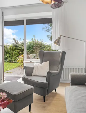 Wohnzimmer mit grauem Sessel, Sofa, Stehlampe und offenem Zugang zum Garten.