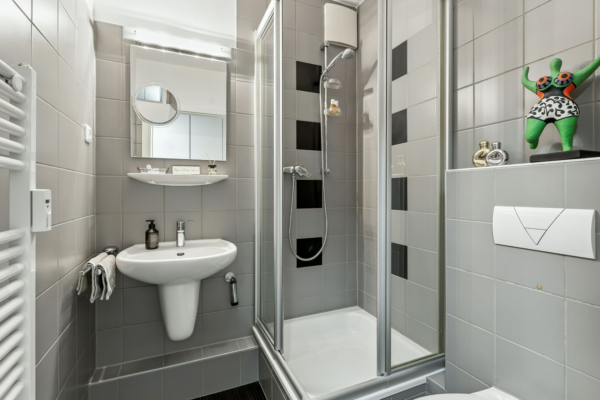 Modernes Badezimmer mit Dusche, Waschbecken, Spiegel und grauen Fliesen.