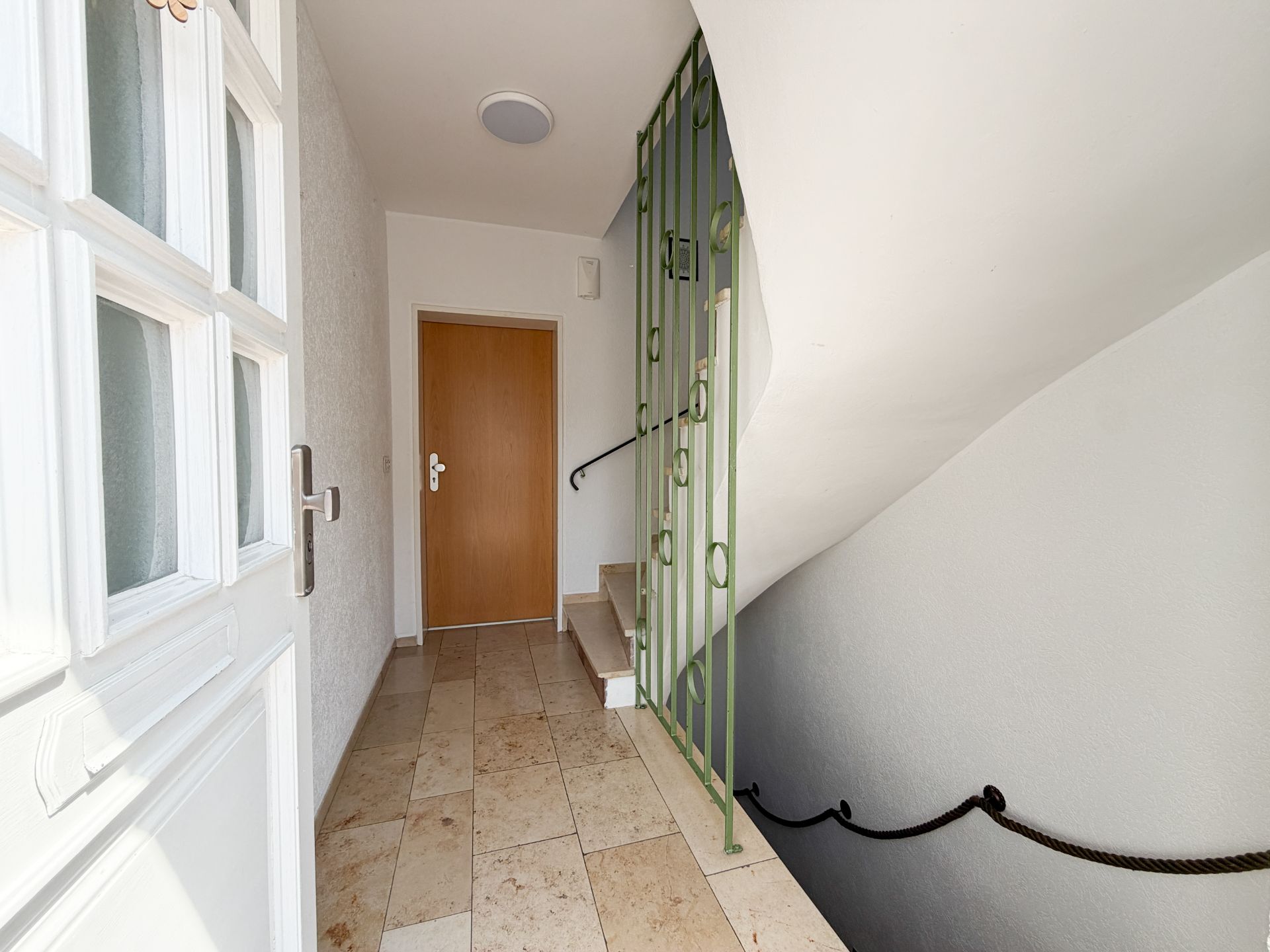 Flur mit Treppe, brauner Tür und weißer Wand in einem Wohnhaus.