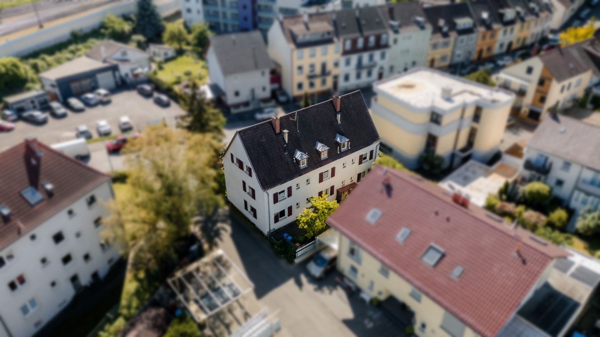 Luftaufnahme eines mehrstöckigen Wohngebäudes mit dunklem Dach und weißen Fassaden.