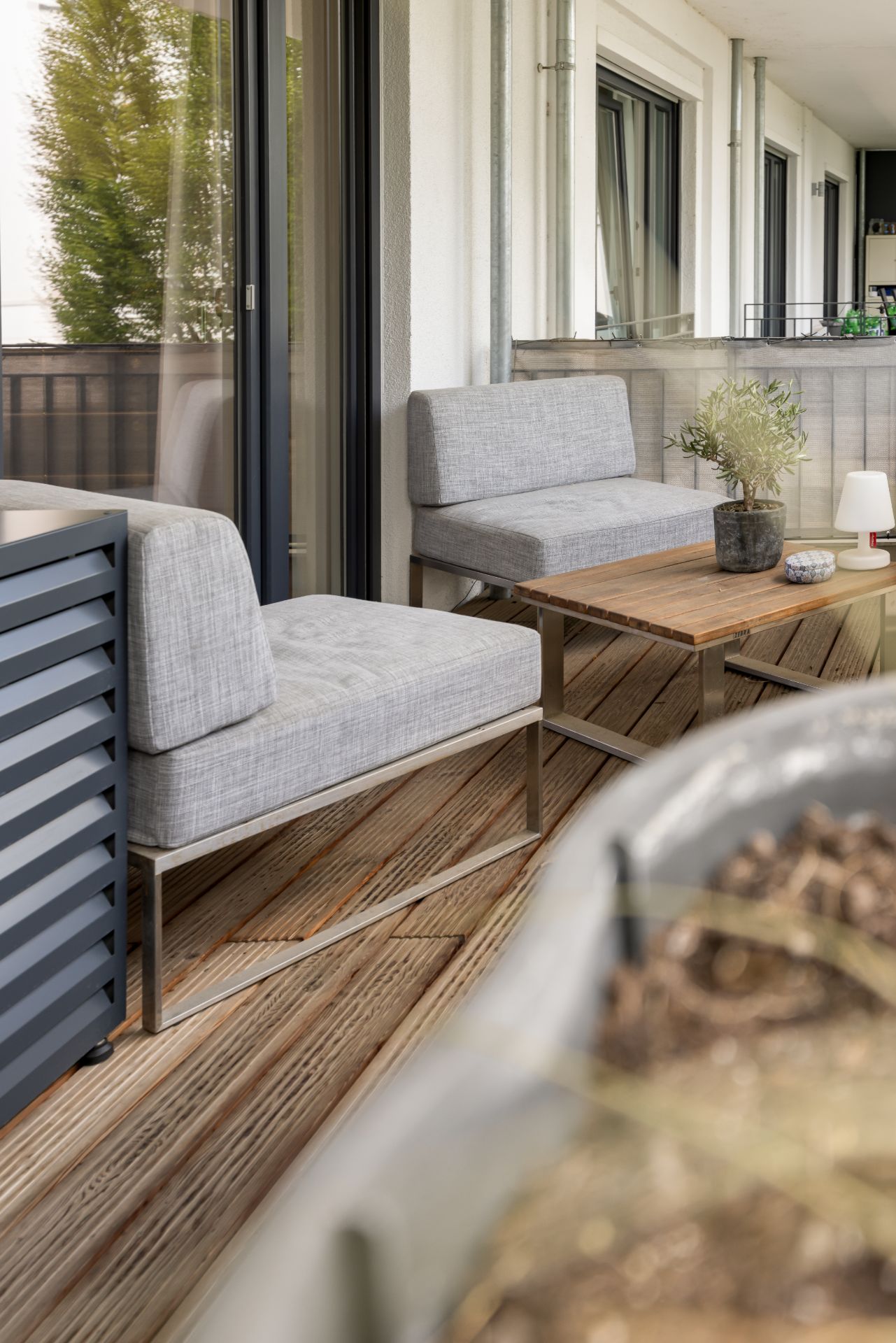 Balkon mit zwei grauen Sitzbänken, Holztisch, Pflanze und Holzfußboden.