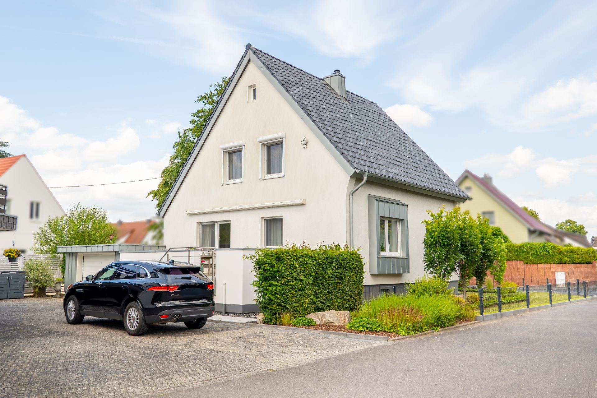 Modernes Einfamilienhaus mit schwarzem Auto davor und gepflegtem Garten.