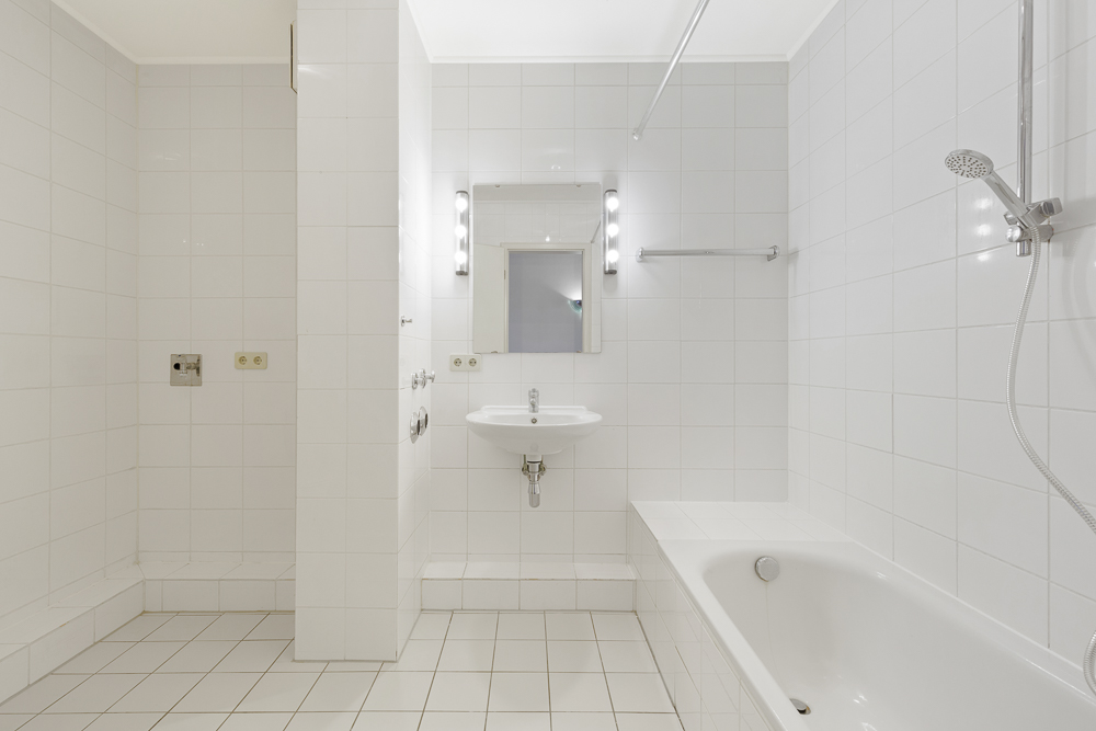 Helles Badezimmer mit Badewanne, Dusche, Waschbecken und beleuchtetem Spiegel.