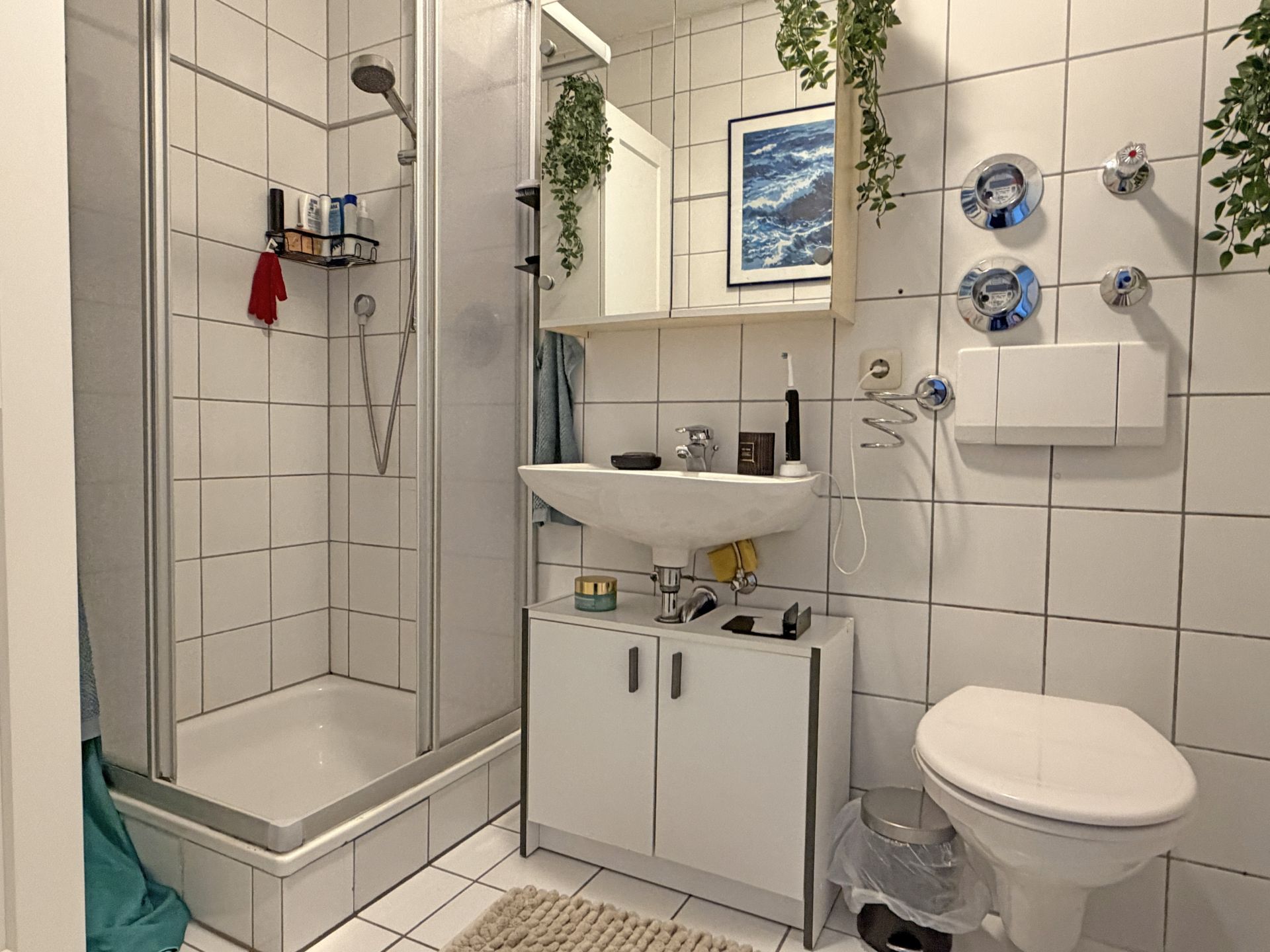 Modernes Badezimmer mit Dusche, Waschbecken, Spiegel, WC und weißen Fliesen.