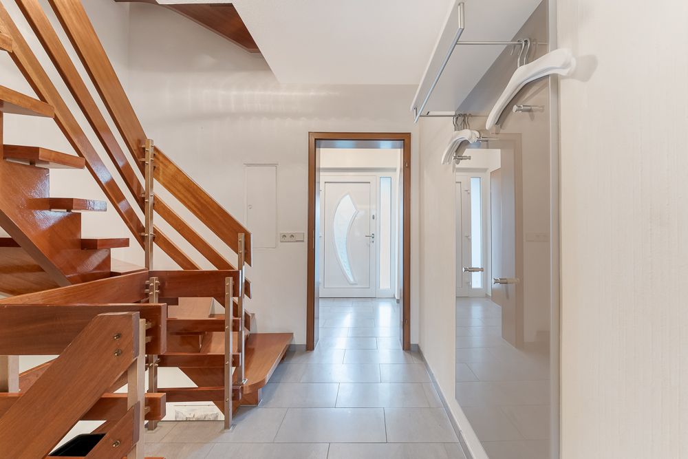Flur mit Holztreppe, weißer Haustür und Garderobe mit Spiegel im Innenbereich.