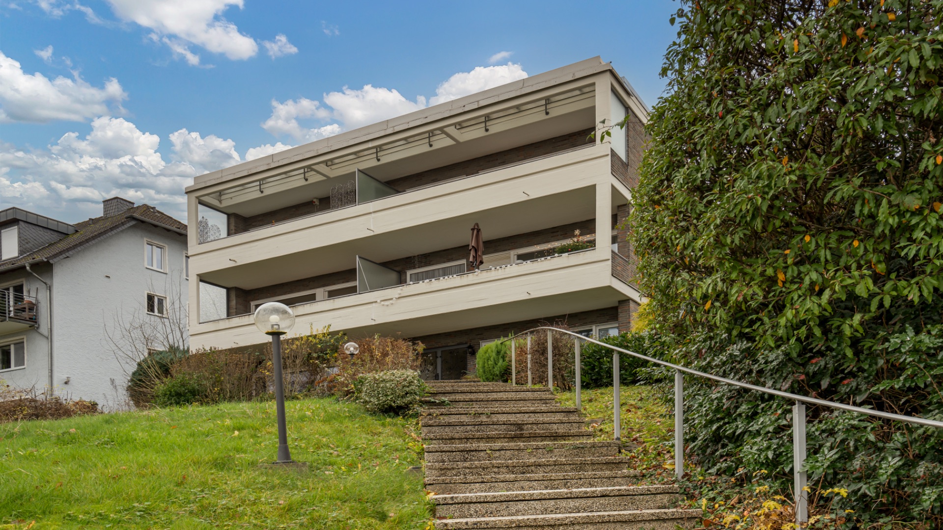 Treppenaufgang zu einem modernen Mehrfamilienhaus mit Balkonen und umliegendem Grün.