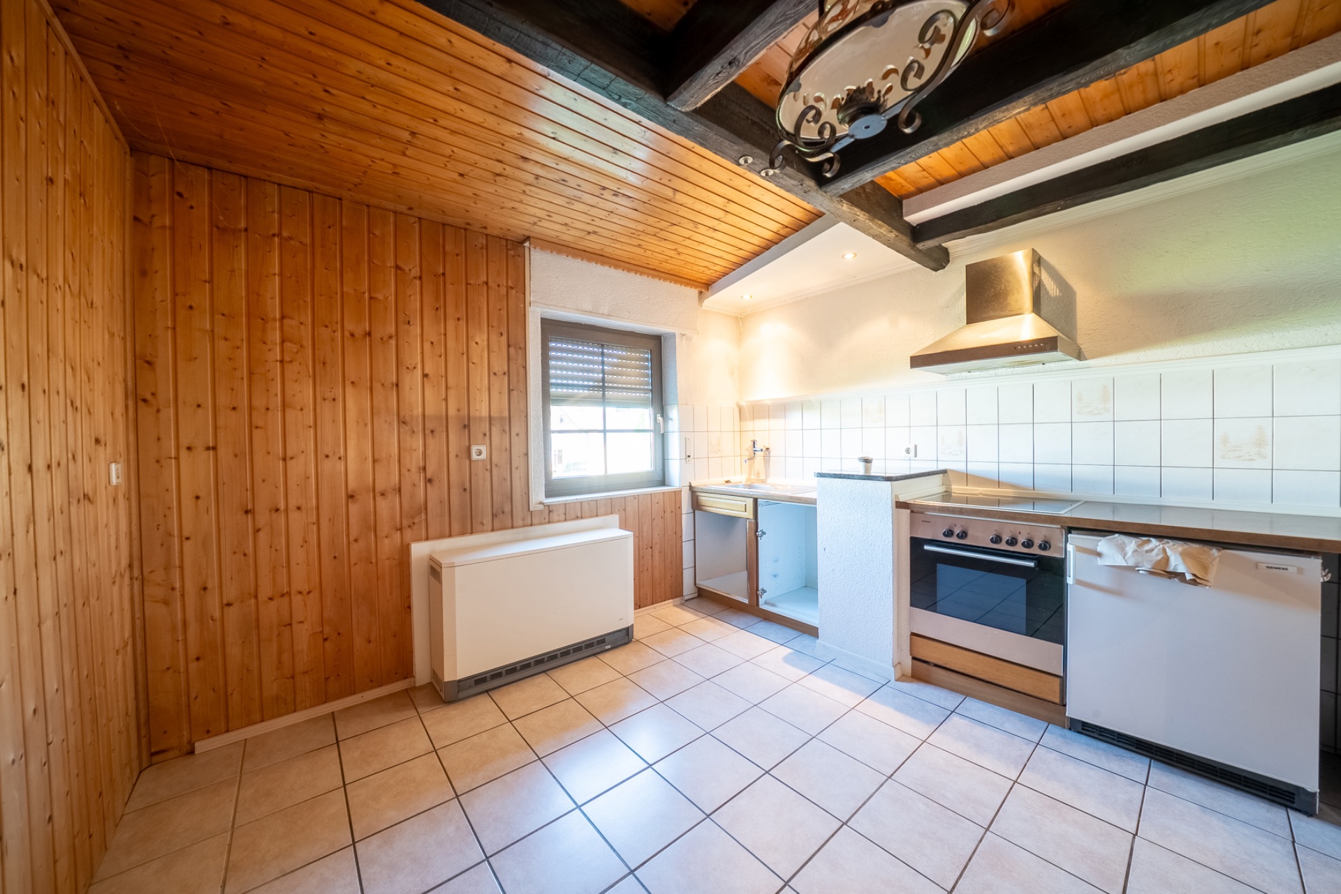 Küche mit Holzdecke, Fliesenboden, Fenster, Herd und Spüle.