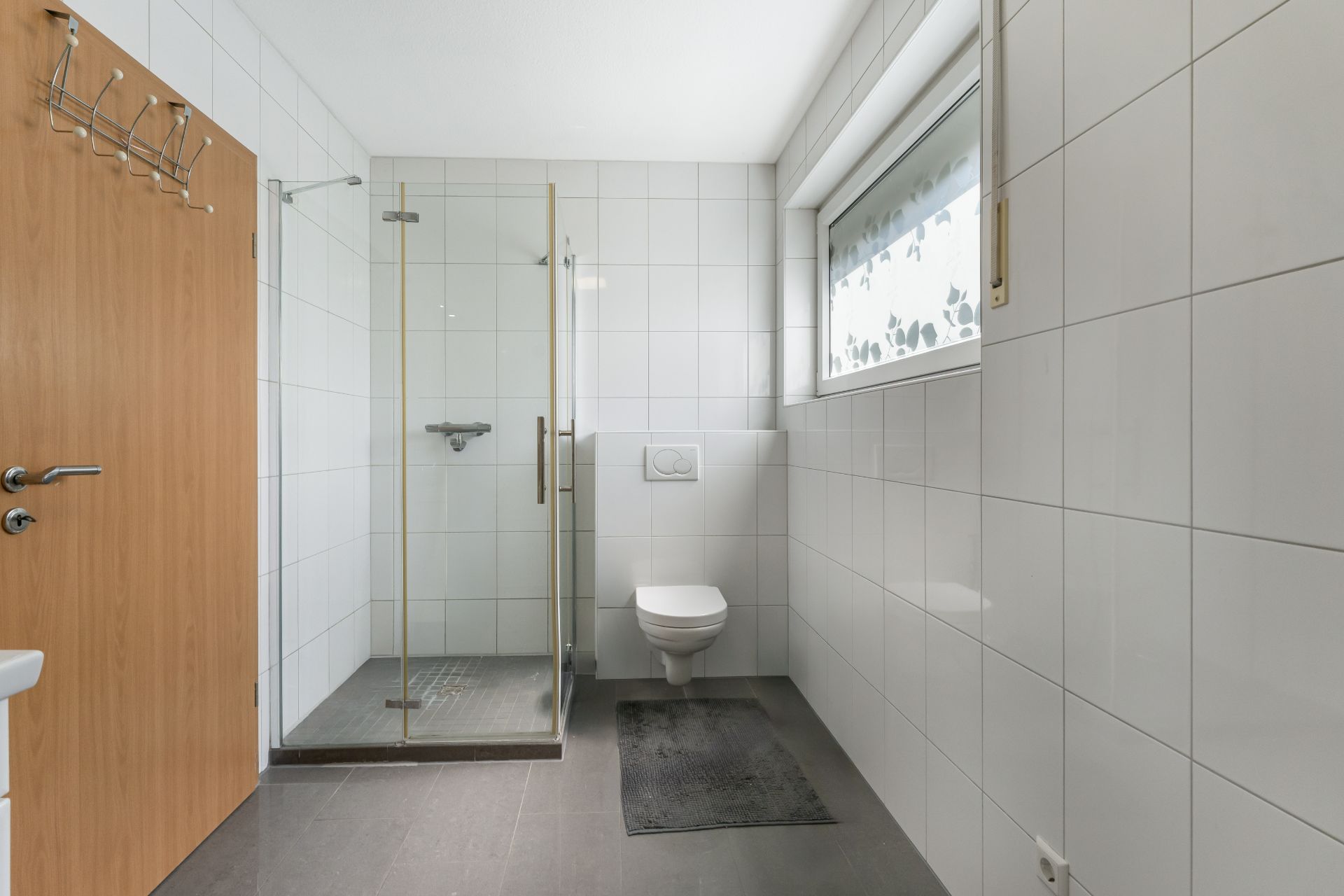 Modernes Bad mit gefliesten Wänden, ebenerdiger Dusche, WC und Fenster.