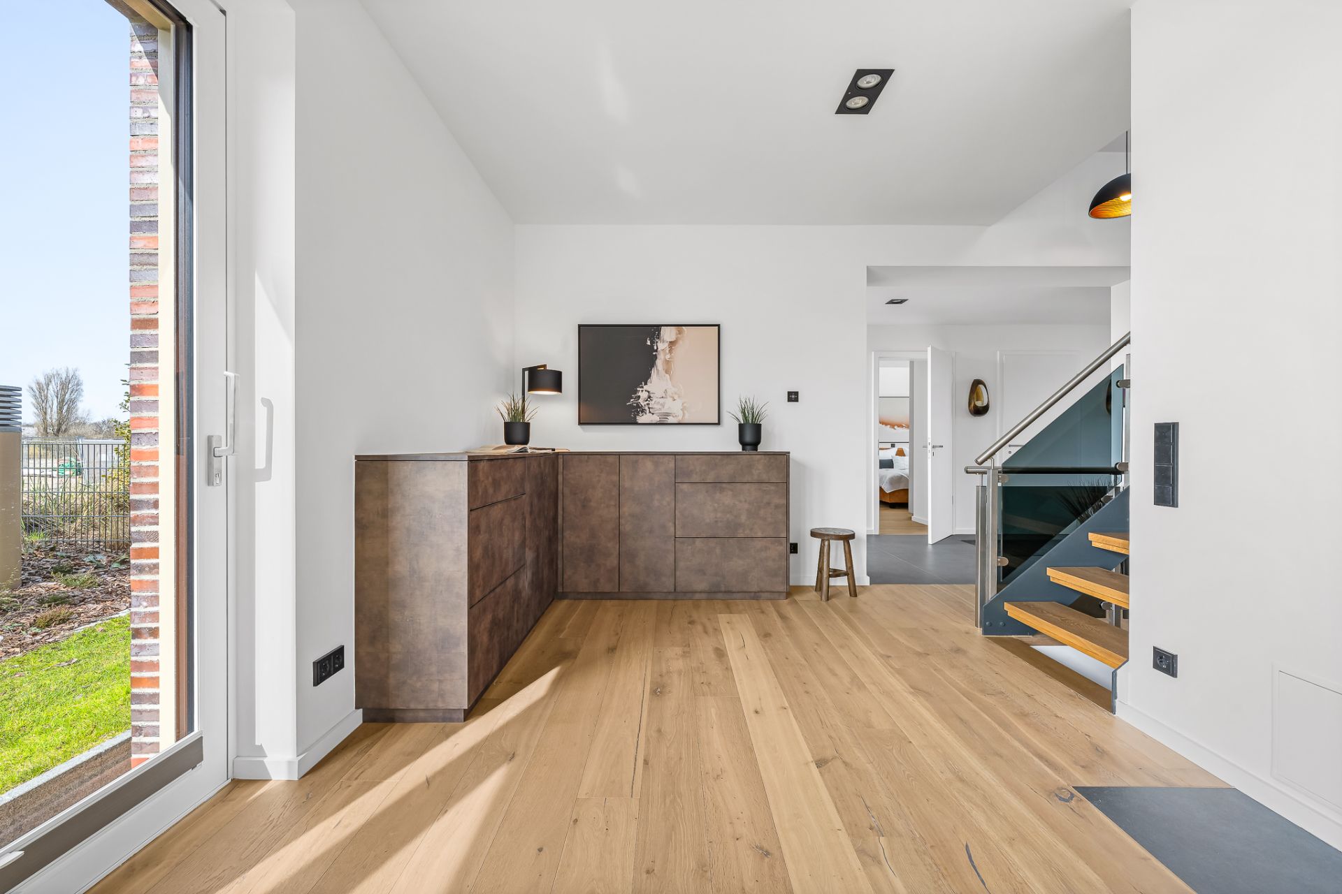 Heller Flur mit Holzboden, einer modernen Kommode und einer offenen Holztreppe.
