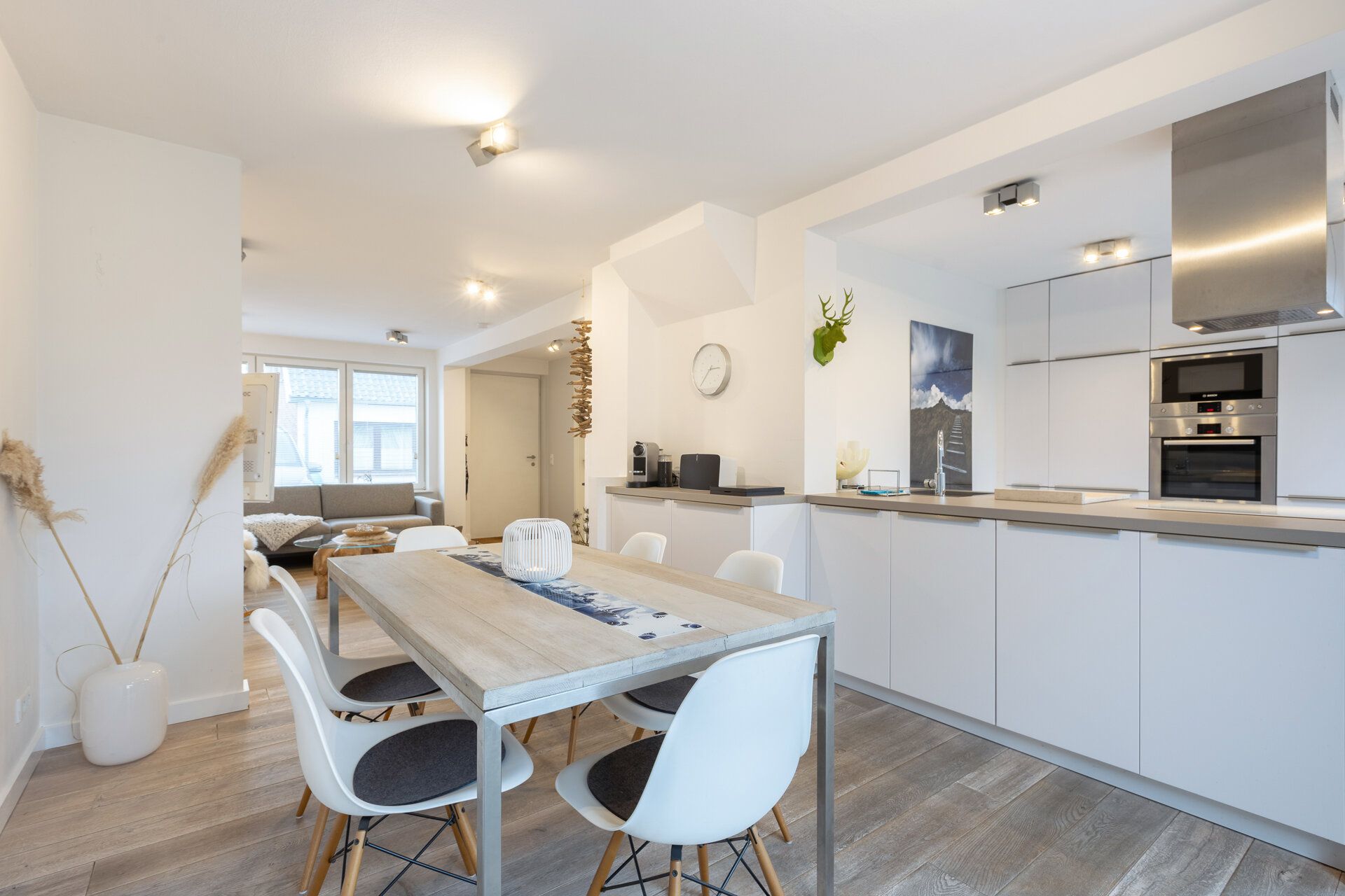 Moderne offene Wohnküche mit Esstisch, weißen Stühlen und großem Fenster.