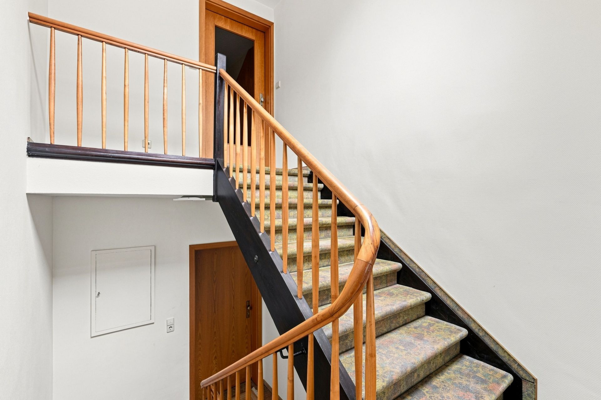Treppe mit Holzgeländer in einem hellen Flur, Türen im oberen und unteren Bereich sichtbar.