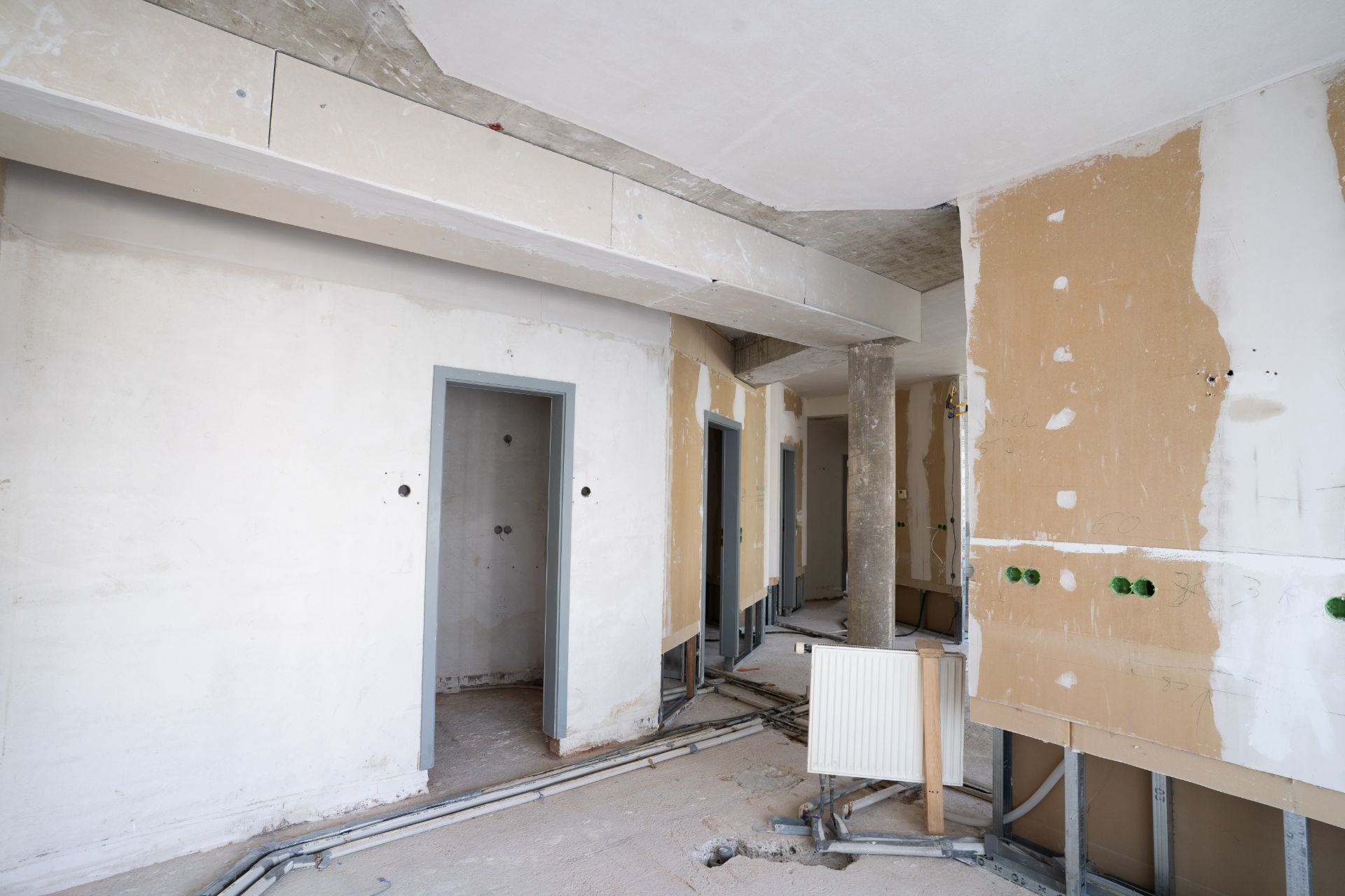Leerer Raum in einer Wohnung im Rohbau mit sichtbaren Leitungen und unverputzten Wänden.