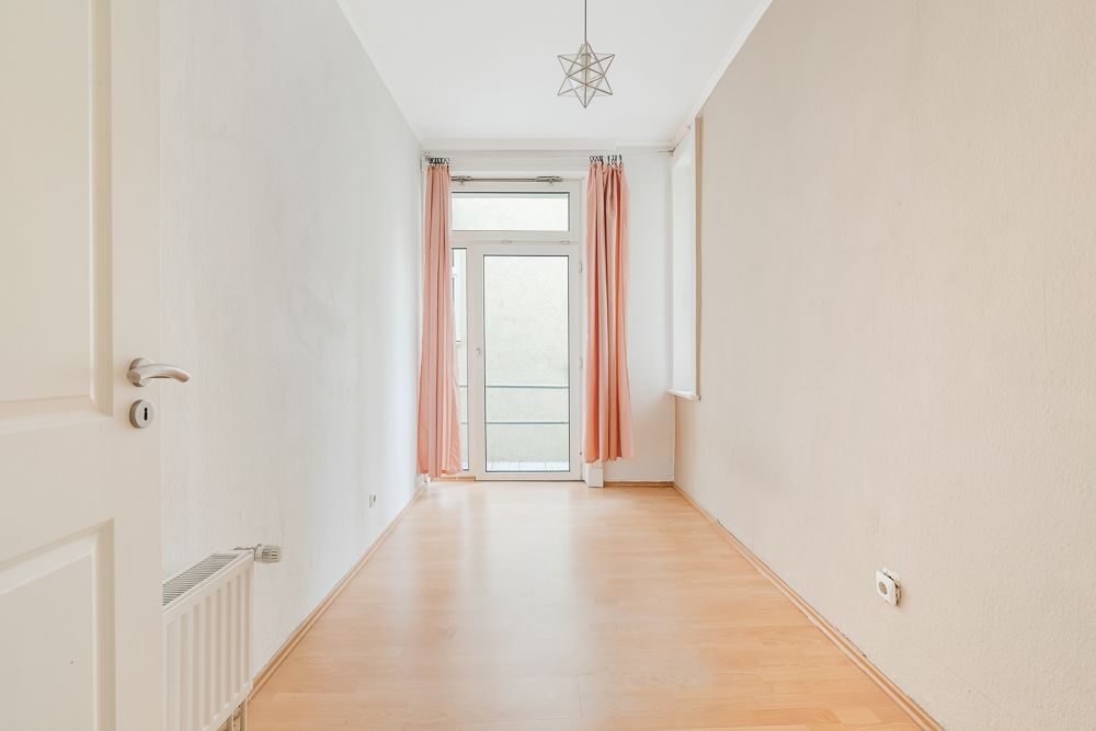 Heller, leerer Raum mit Holzfußboden, Fenster und Glastür, rosa Vorhänge.