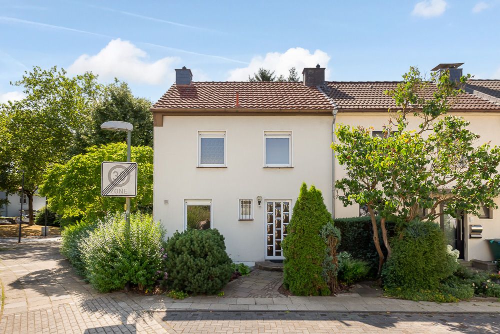 Vorderansicht eines zweistöckigen Reihenhauses mit Garten und Gehweg.