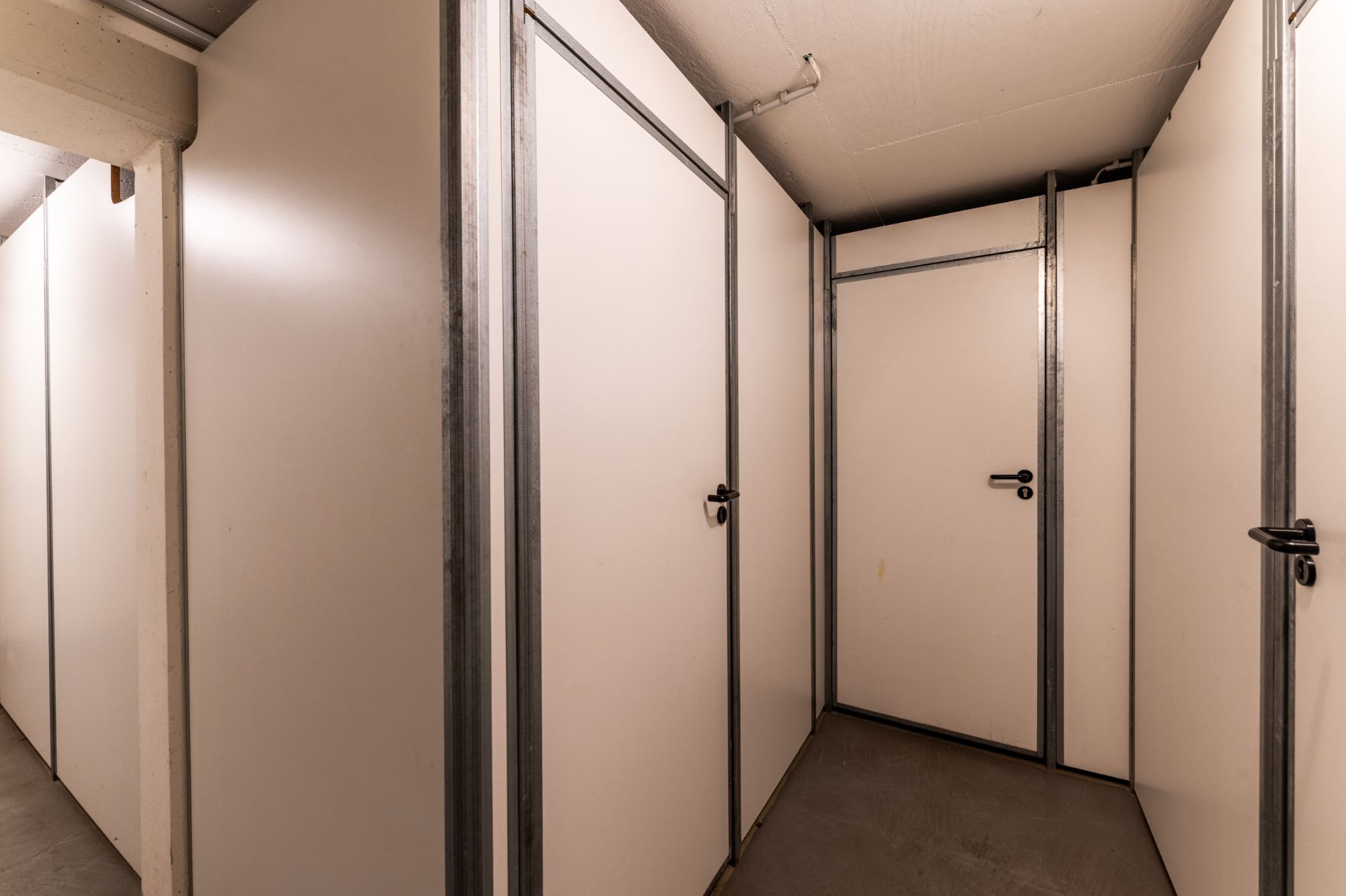 Flur mit mehreren weißen Kellertüren und Metallrahmen in einem Wohnhaus.