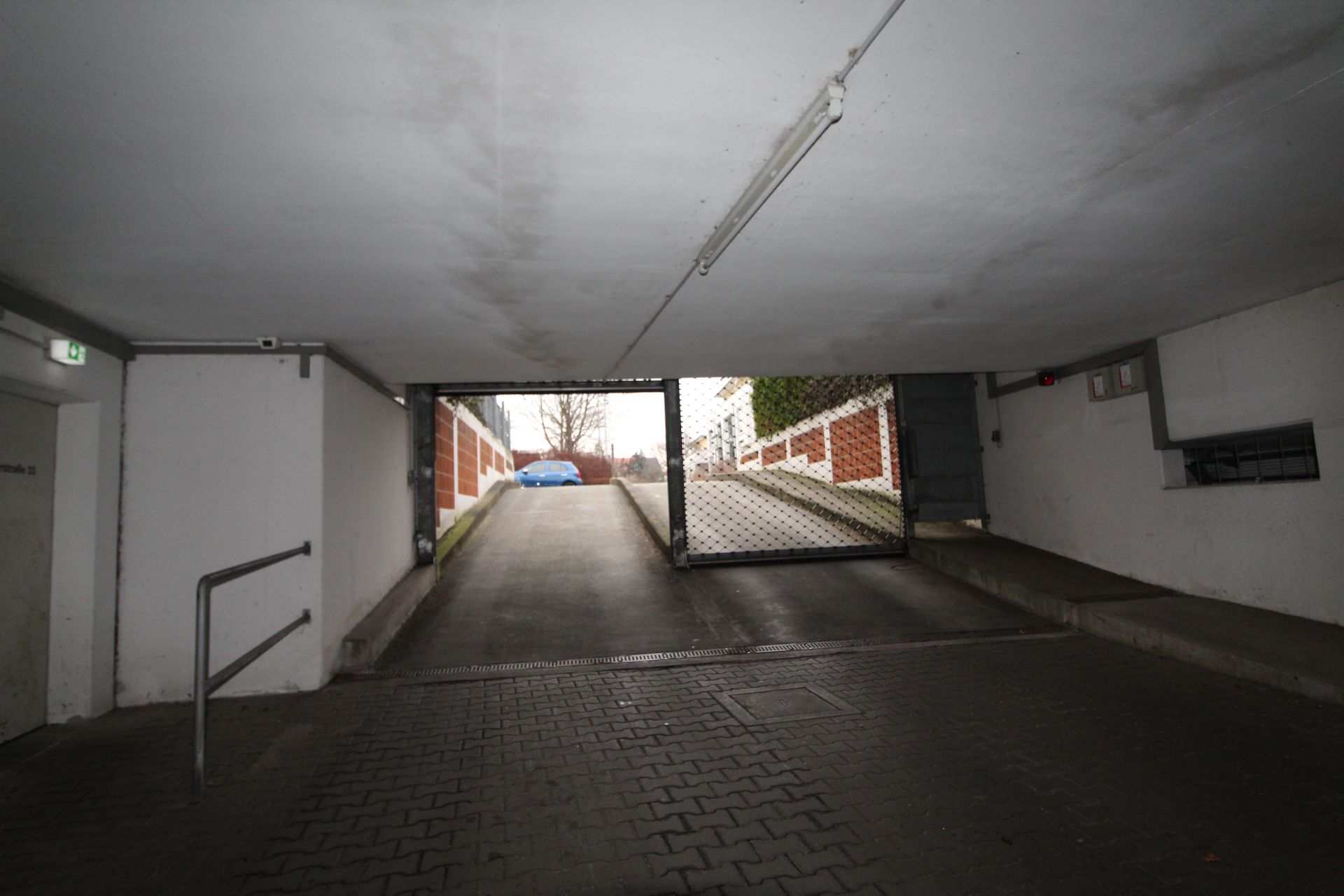 Einfahrt zur Tiefgarage mit offenem Tor und Rampe nach draußen.