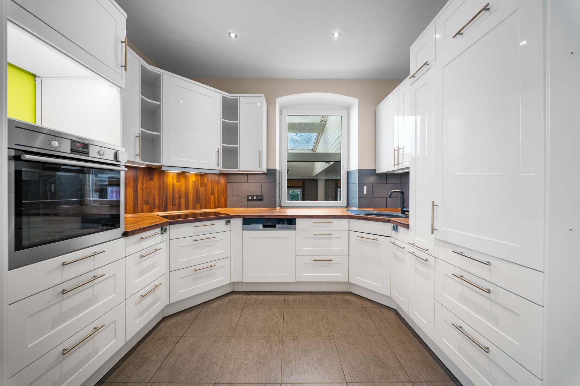 Moderne Küche mit weißen Schränken, Holzarbeitsplatten und großem Fenster.