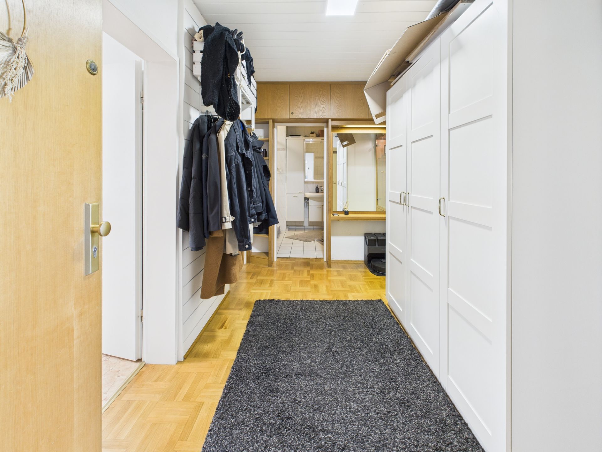 Heller Flur mit Garderobe, weißen Schränken und Teppich auf Holzboden.
