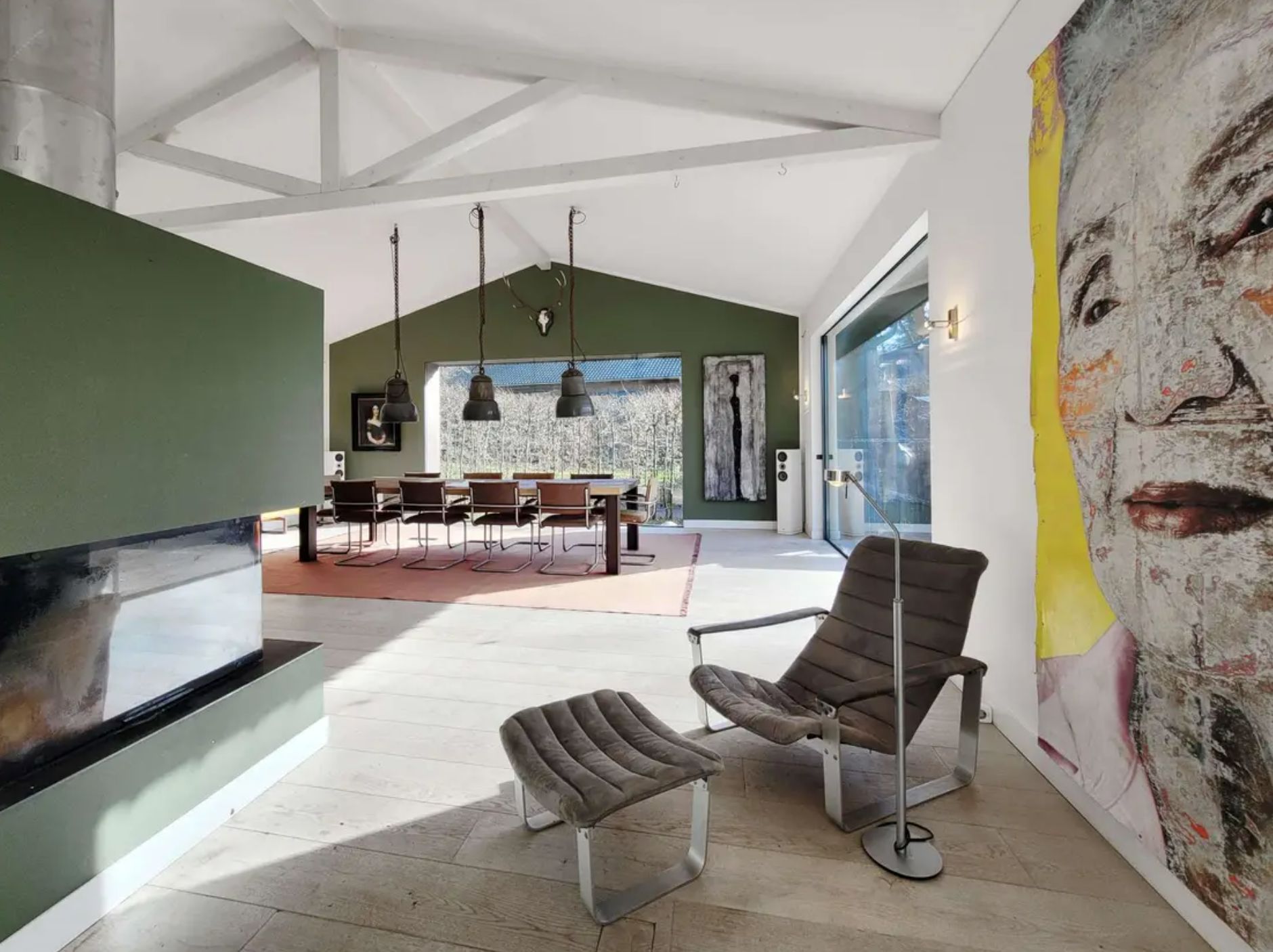 Heller Wohnraum mit Sessel, Kamin, großem Esstisch und moderner Kunst an der Wand.