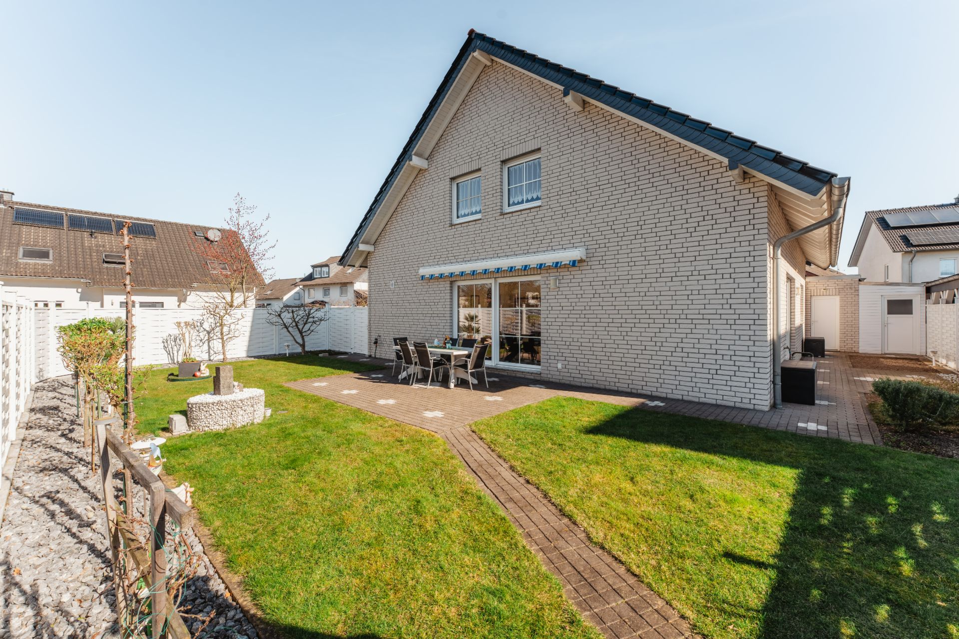 Gepflegter Garten mit Terrasse und Sitzgruppe hinter einem Einfamilienhaus mit weißer Fassade.