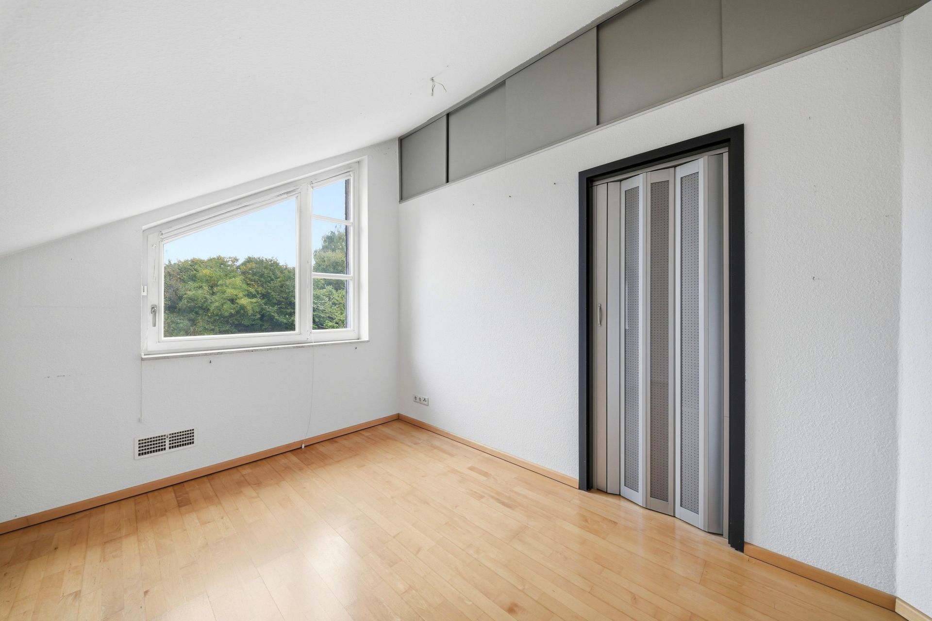 Leerstehendes Zimmer mit Holzfußboden, Fenster und Falttür.