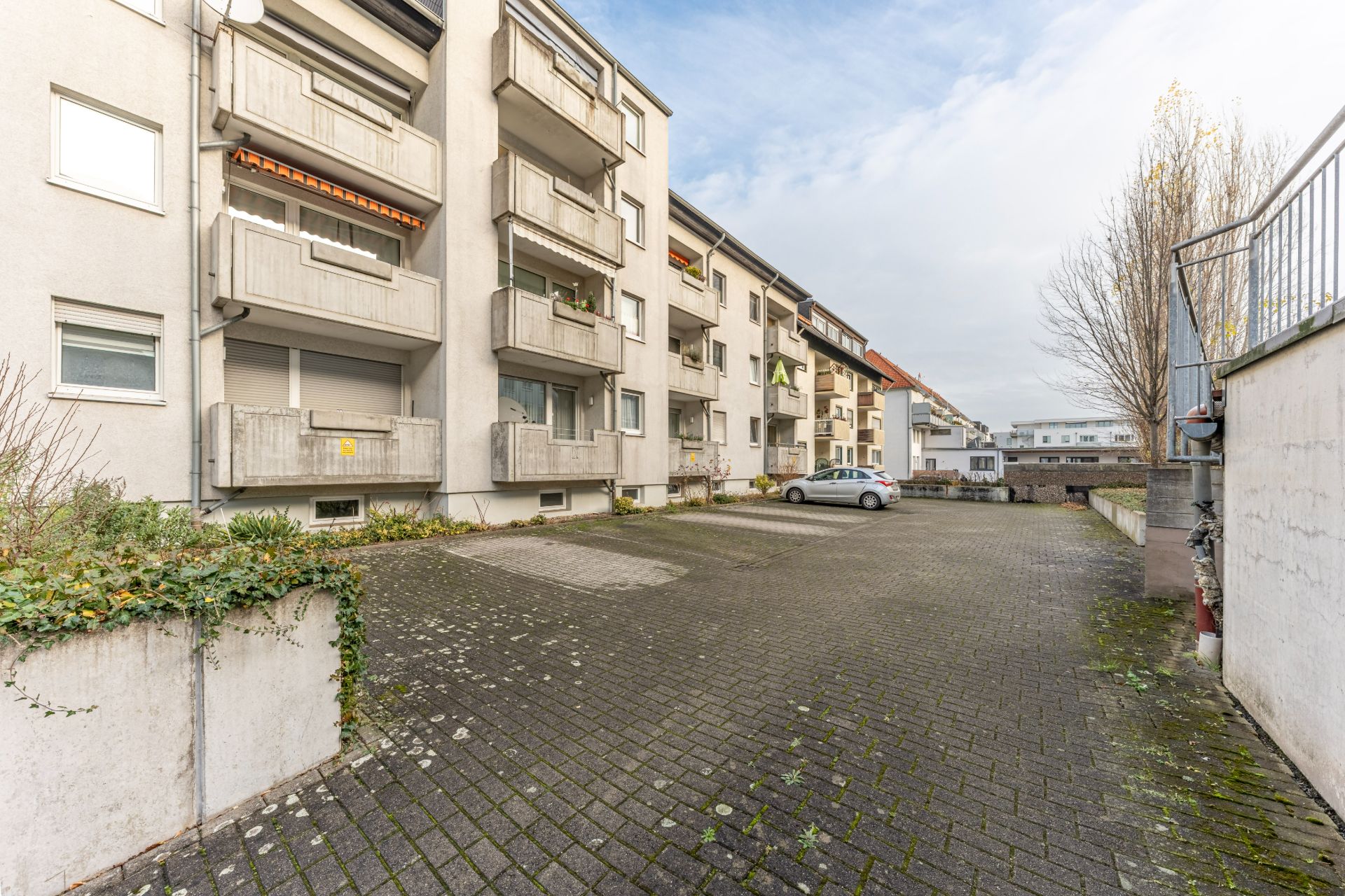 Gepflasterter Parkplatz vor einem mehrstöckigen Wohnhaus mit Balkonen.