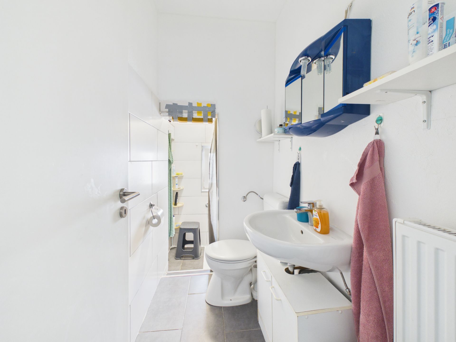 Helles Badezimmer mit Waschbecken, Spiegel, Toilette und Handtüchern an der Wand.
