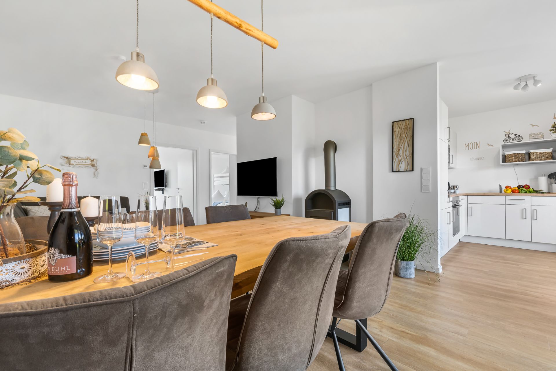 Moderner Essbereich mit Holztisch, gepolsterten Stühlen und offener Küche im Hintergrund.