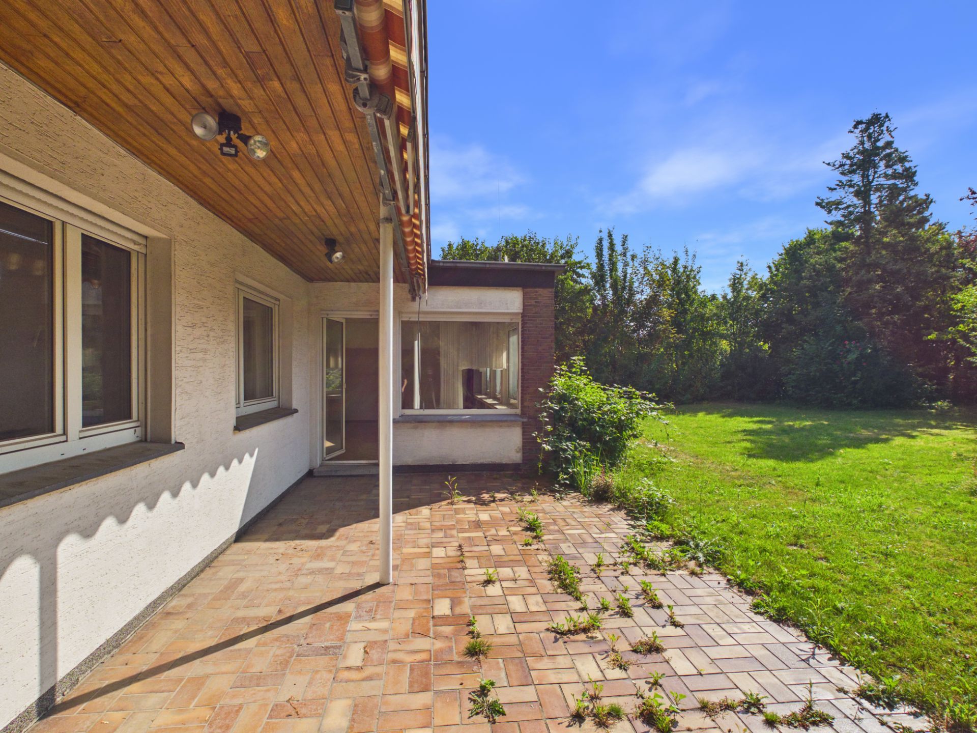 Überdachte Terrasse mit Fliesenboden, blick auf Garten und Fensterfront.