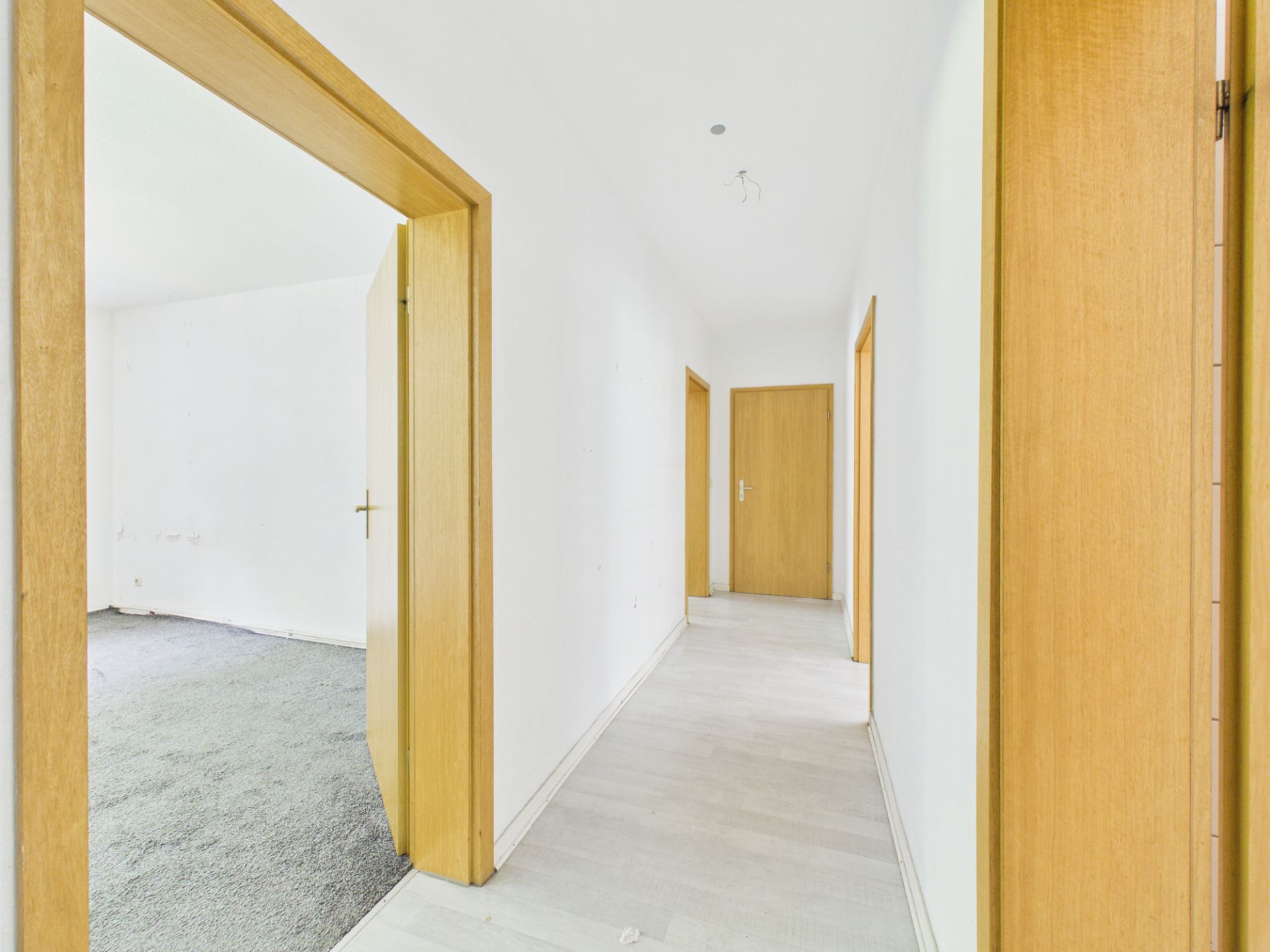 Heller Flur mit Holztüren und weißen Wänden in einer Wohnung.