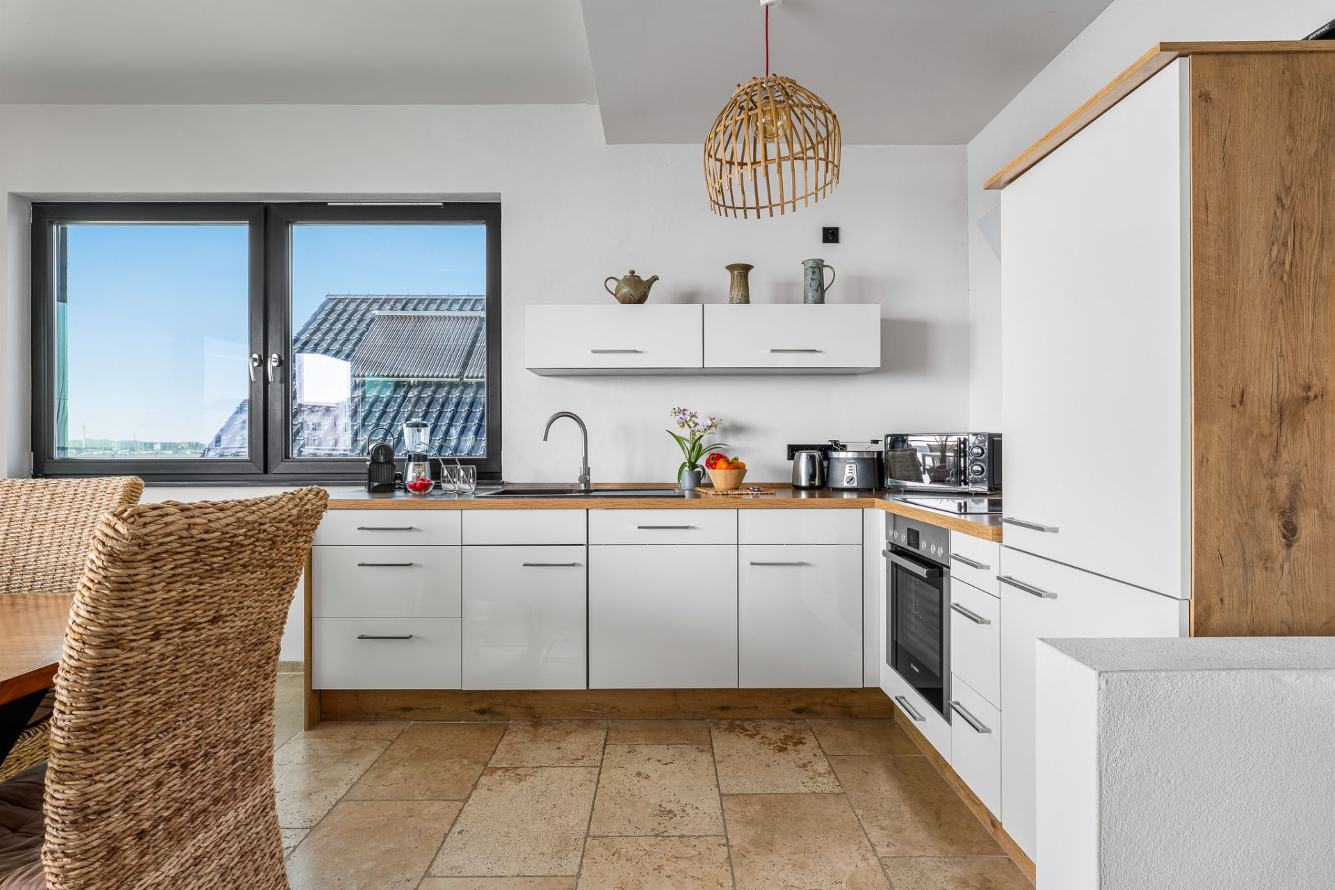 Moderne Küche mit weißen Schränken, Holzarbeitsplatte und großem Fenster.