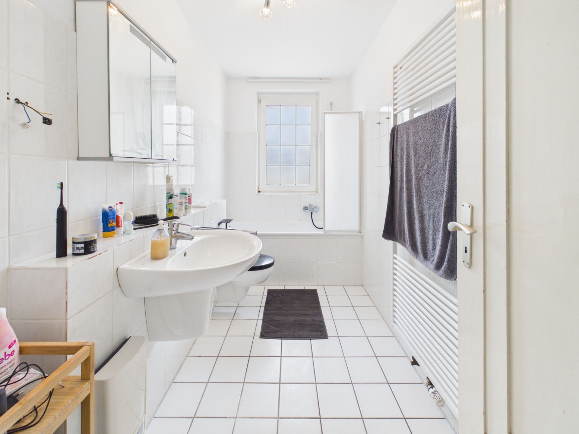 Helles Badezimmer mit Badewanne, Waschbecken, Spiegel und Handtuchheizkörper.