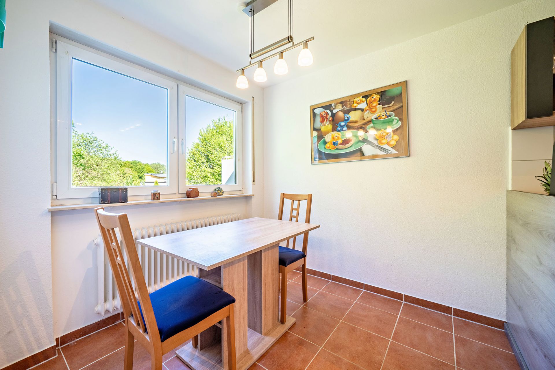 Kleiner Essbereich mit Holztisch, zwei Stühlen und großem Fenster, Gemälde an der Wand.