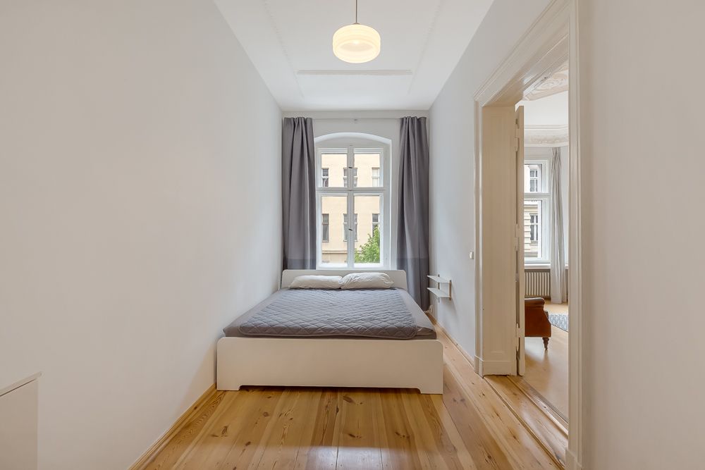 Schlafzimmer mit Doppelbett, Holzfußboden und großem Fenster mit grauen Vorhängen.
