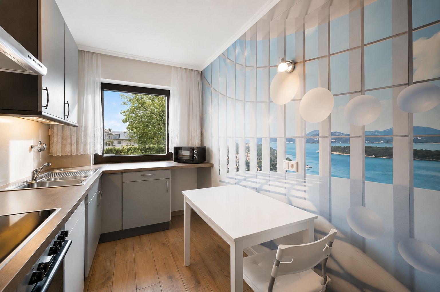 Helle Küche mit grauen Schränken, Holzboden, Wandbild und Fenster mit Blick ins Grüne.