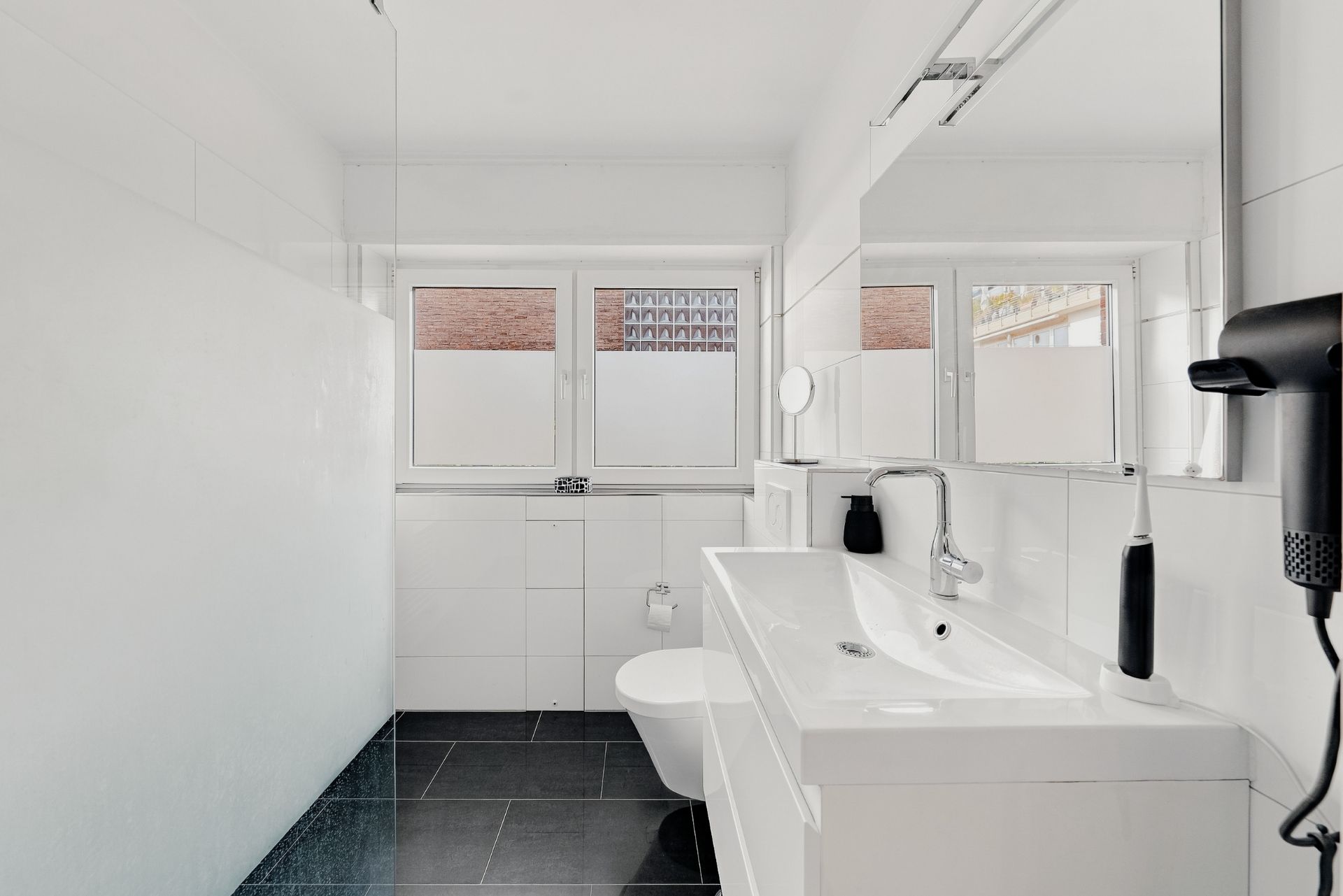 Modernes Badezimmer mit weißem Waschbecken, Spiegel, Toilette und drei Fenstern.