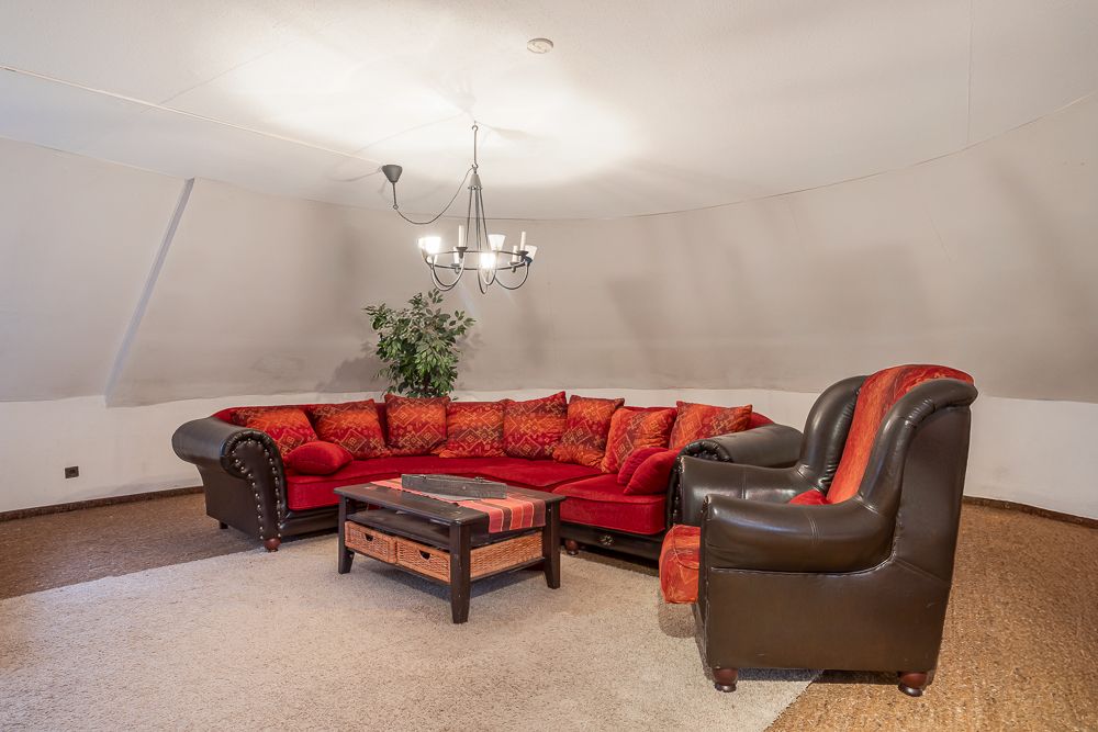 Wohnzimmer mit rotem Ecksofa, braunem Sessel, Couchtisch und Hängelampe.
