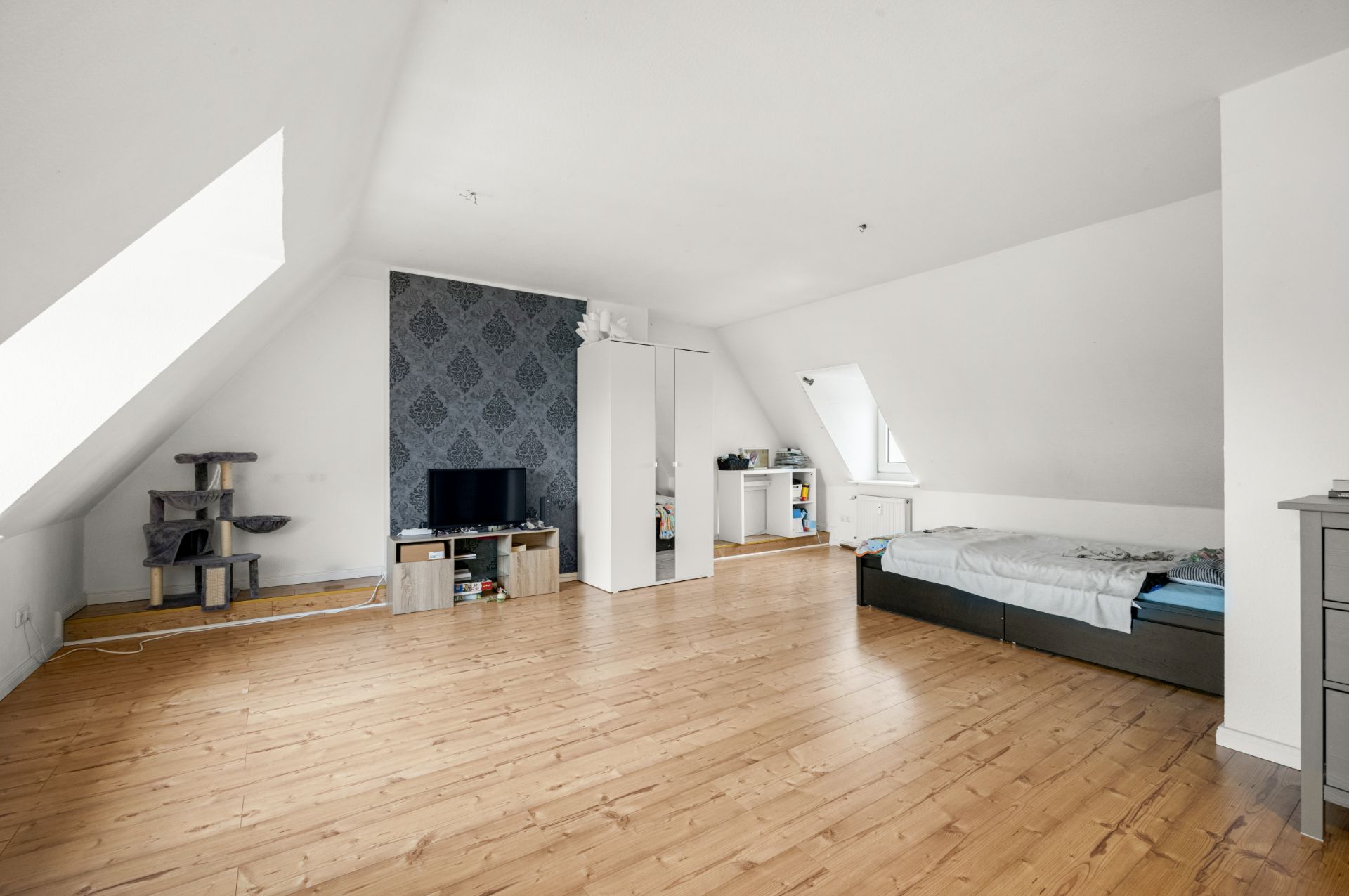 Helles Schlafzimmer mit Holzfußboden, Bett, Fernseher, Schrank und Dachschrägen.