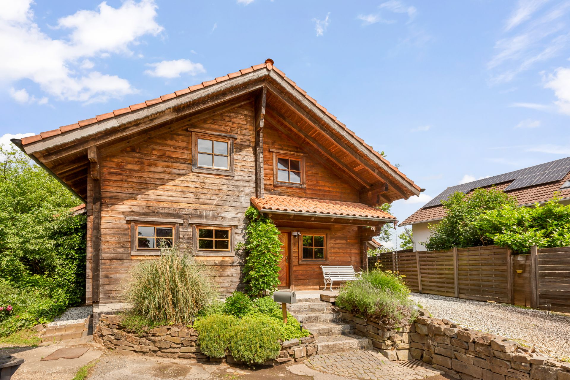 Holzhaus mit Satteldach, kleinem Garten und Bank vor dem Eingang.
