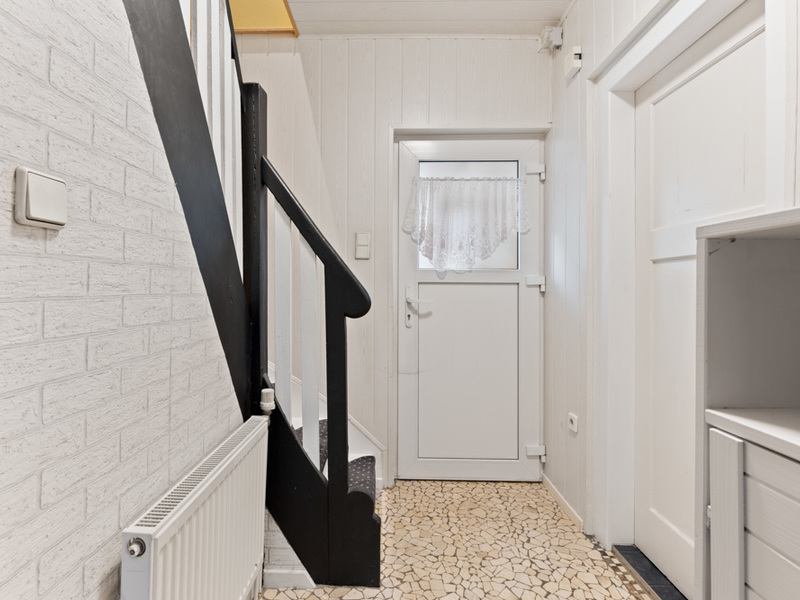 Heller Flur mit weißer Tür, Gardine, Treppe und gemustertem Fliesenboden.