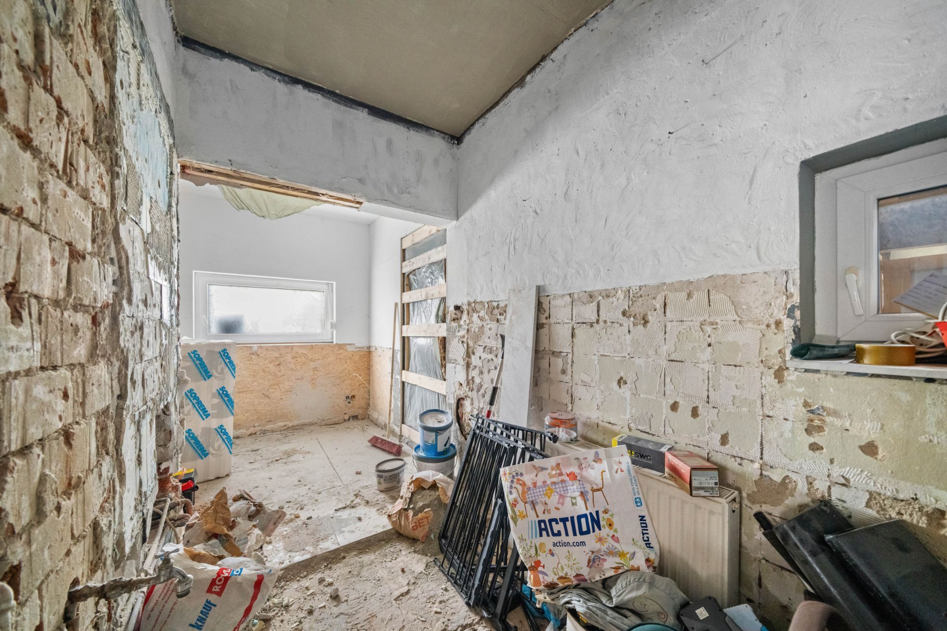 Renovierungsbedürftiger Raum mit freiliegenden Wänden, Baumaterialien und Unordnung.