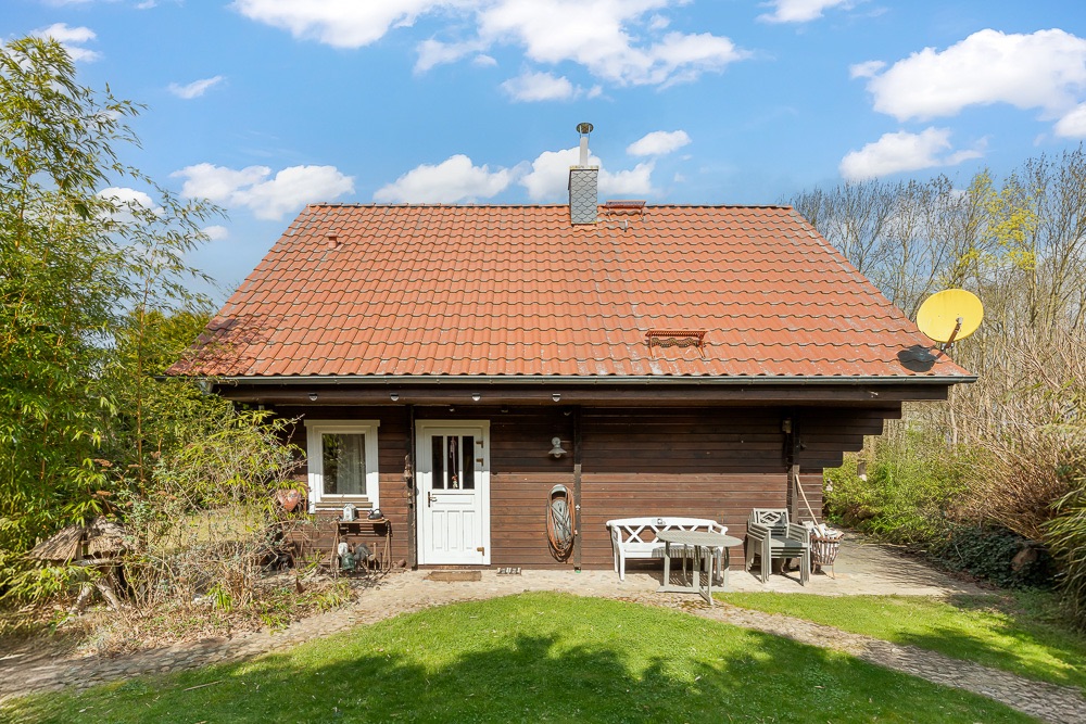 Holzhaus mit rotem Satteldach, weißer Tür und Gartenmöbeln vor dem Eingang.