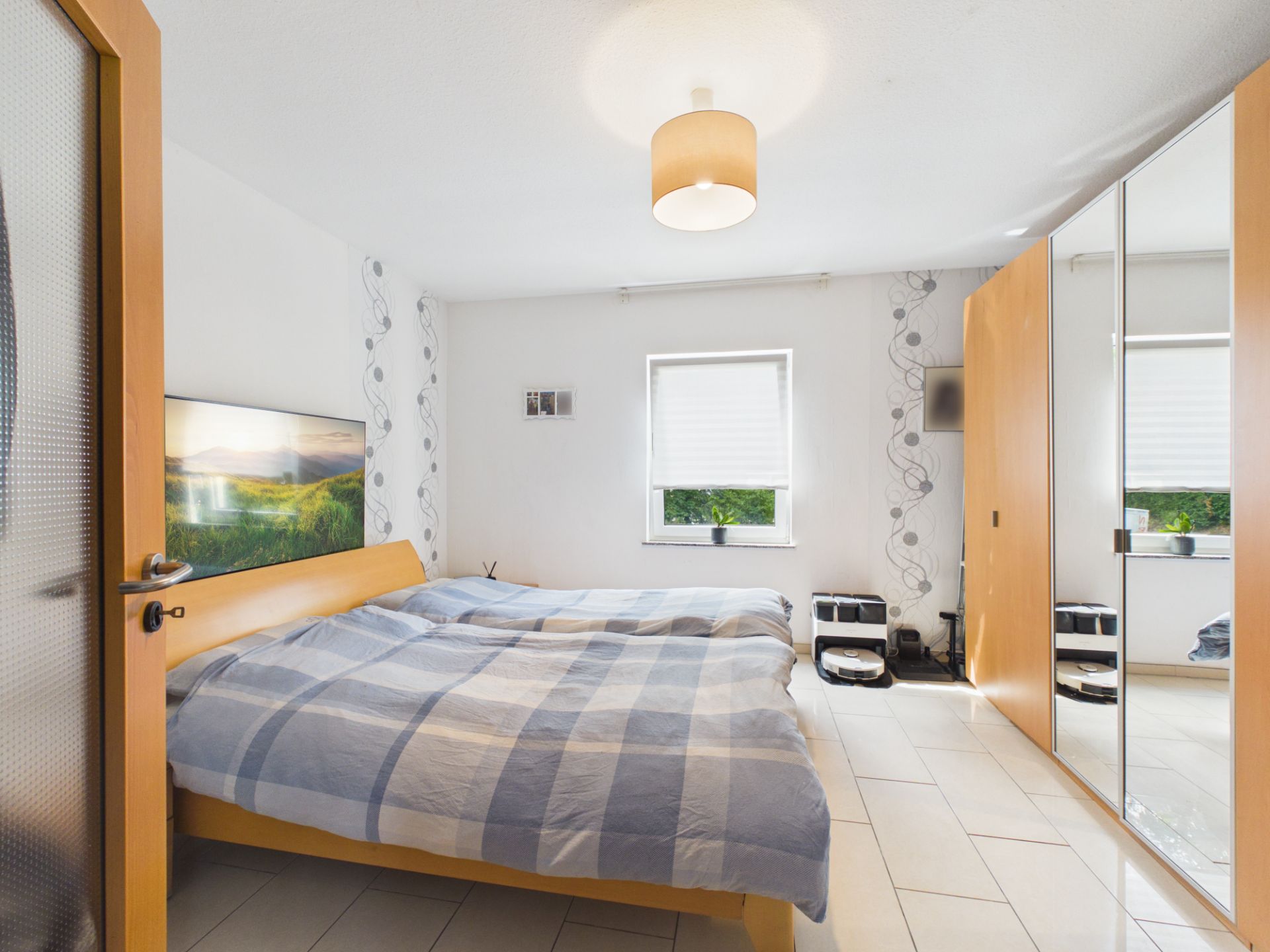 Helles Schlafzimmer mit Doppelbett, Spiegelschrank und Fenster mit Rollladen.