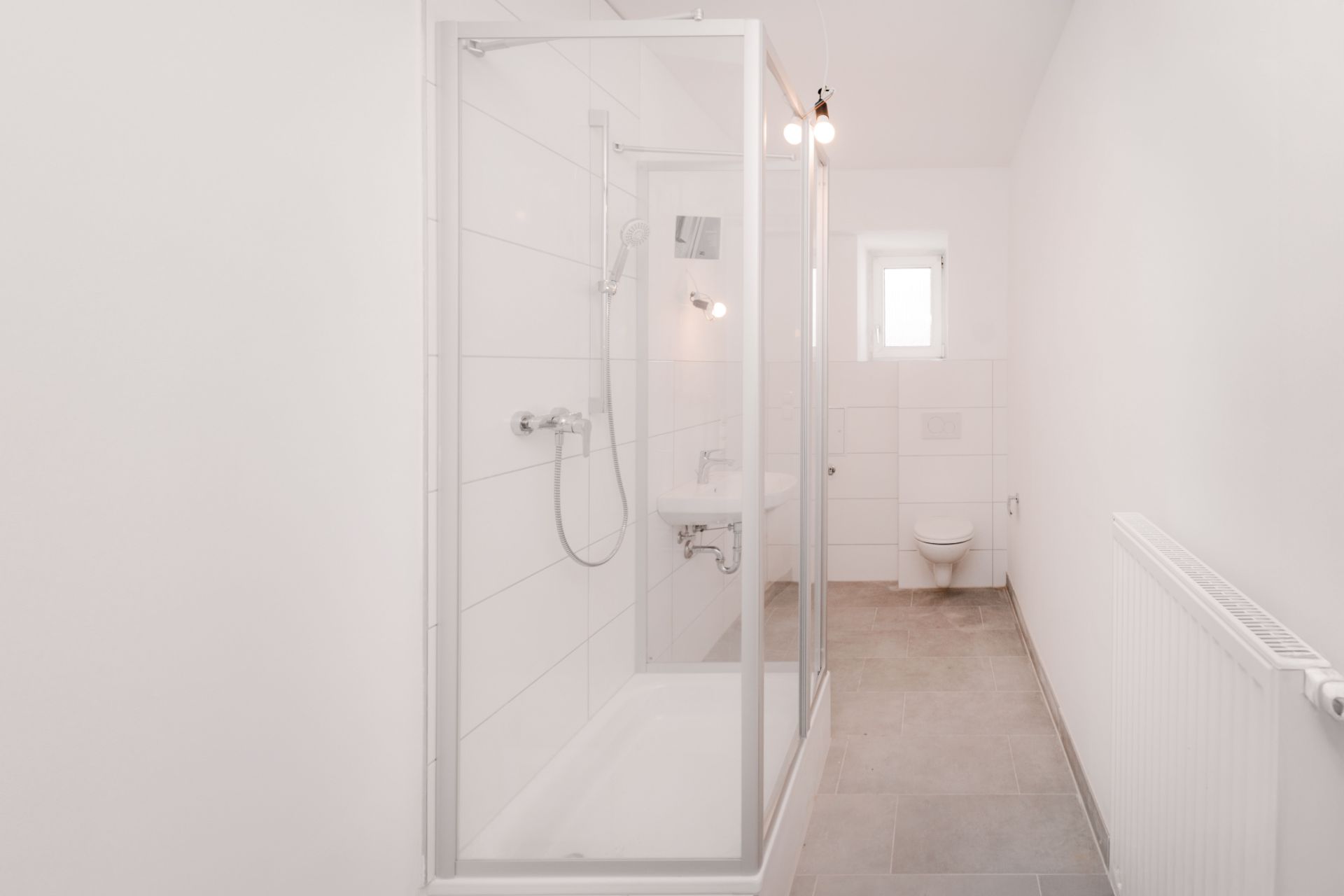 Helles Badezimmer mit Dusche, WC, Waschbecken und kleinem Fenster.
